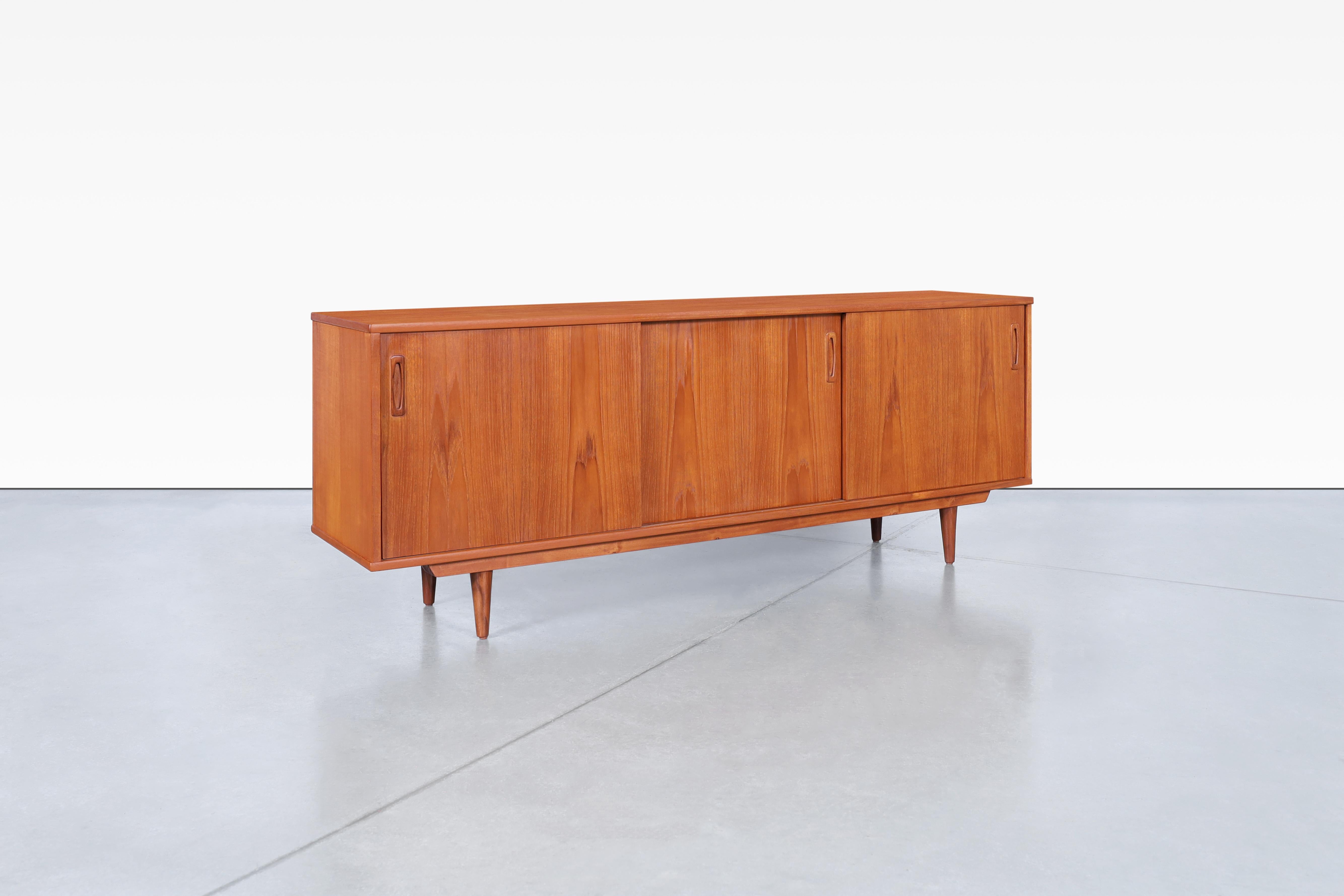 Introducing a stunning Danish modern teak sideboard from the 1960s, beautifully crafted by Dyrlund in Denmark. This exquisite piece features three sleek sliding doors that reveal three adjustable shelves and a convenient pull-out drawer, providing