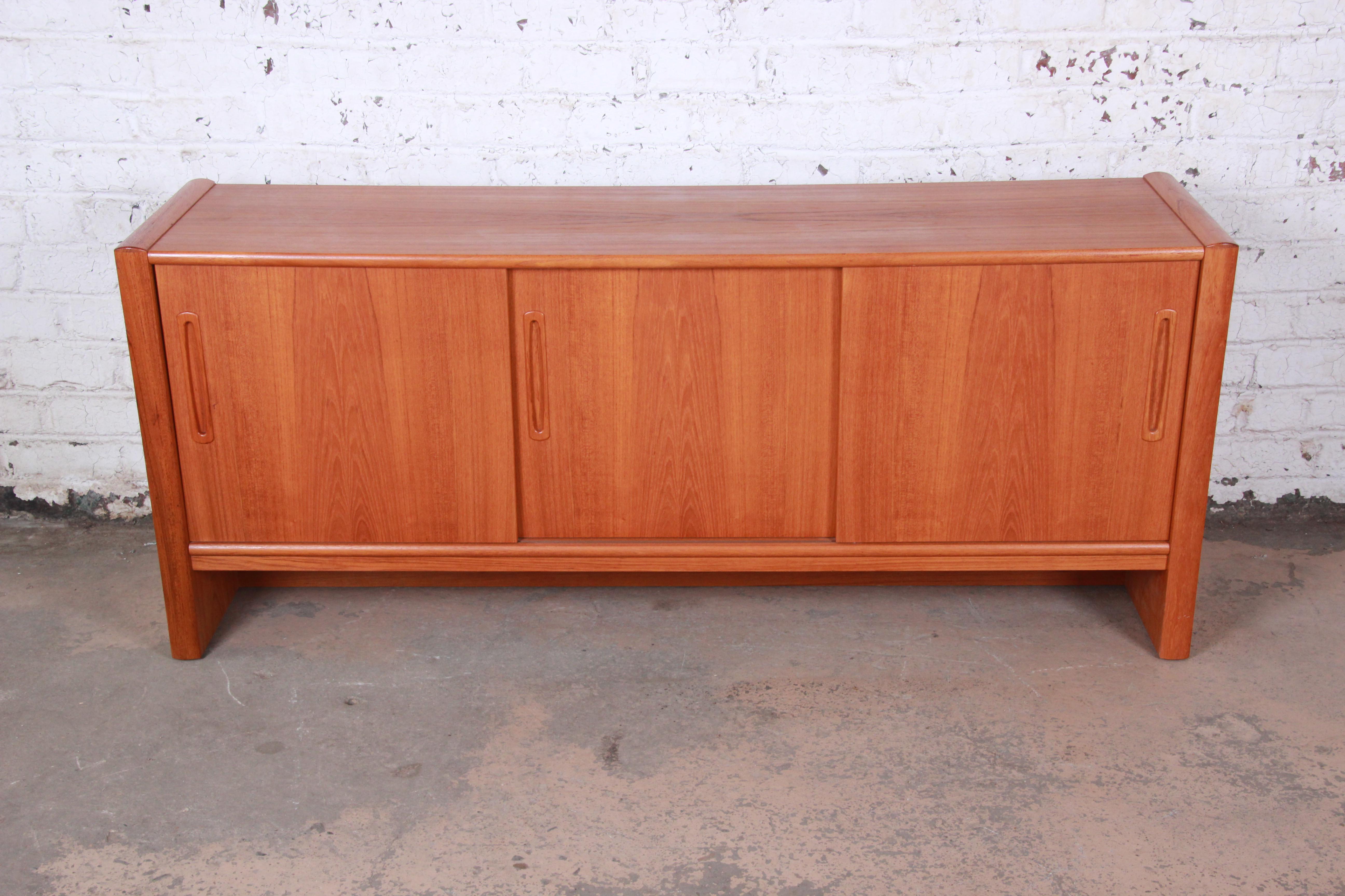 A very nice Danish modern teak sideboard or credenza. The credenza features gorgeous teak wood grain and sleek Danish design. It offers ample storage, with three cabinet spaces behind sliding doors. There are two felt-lined drawers and a single
