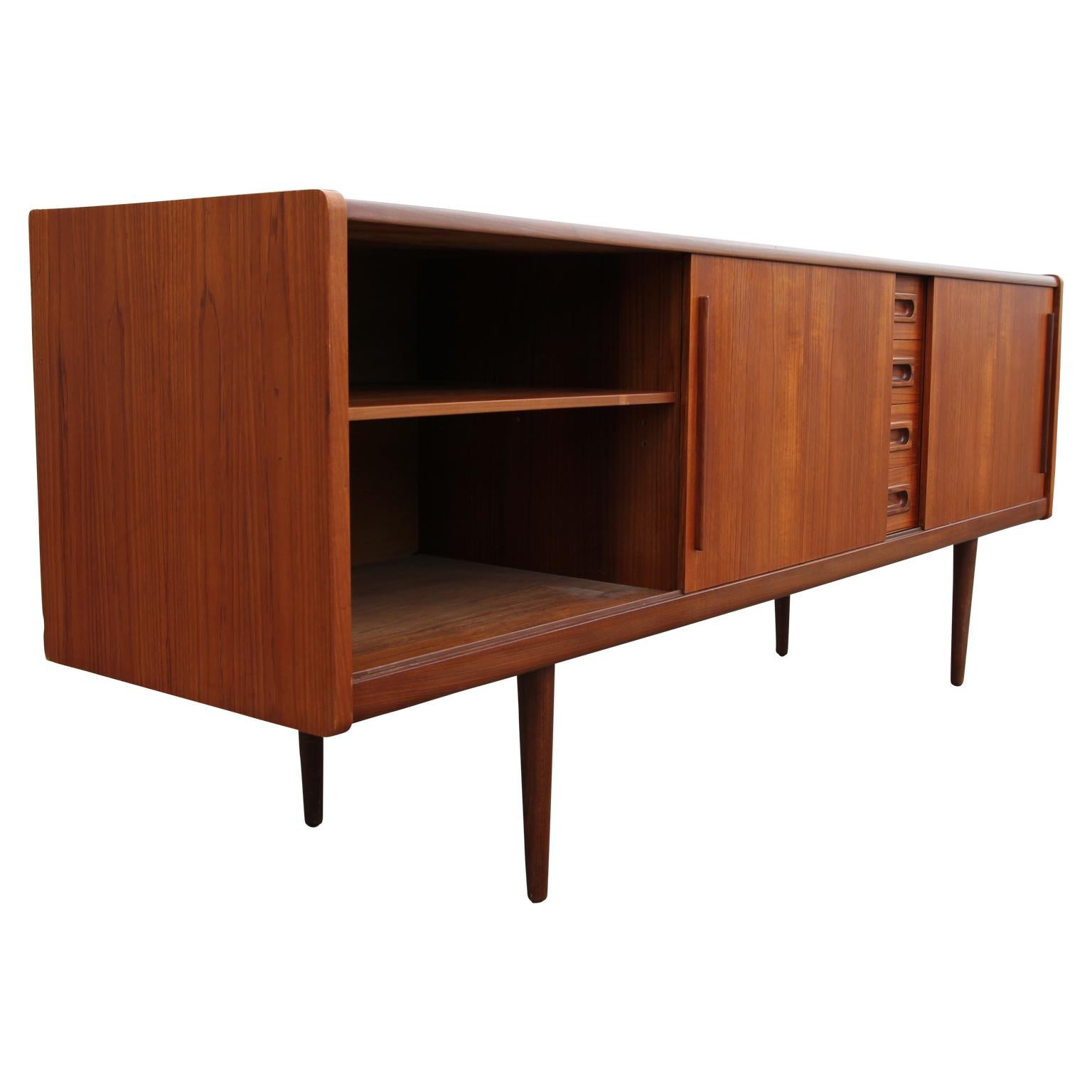 Danish modern teak sideboard or credenza with four central pull out drawers and a set of sliding door cabinets on either side. The clean lines and unique handles make for an elegant, yet functional storage space.