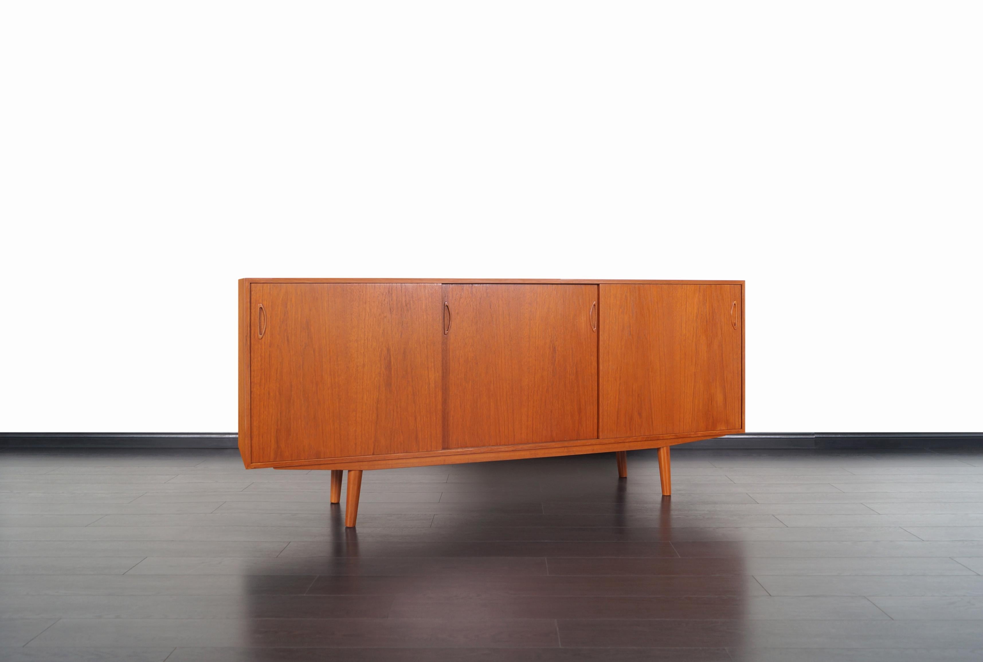 Danish modern teak credenza manufactured in Denmark, circa 1960s. The credenza consist of a sturdy teak wood case that sits on four tapered legs. Features four sliding doors with sculptural pulls that opens up to three sections, revealing two