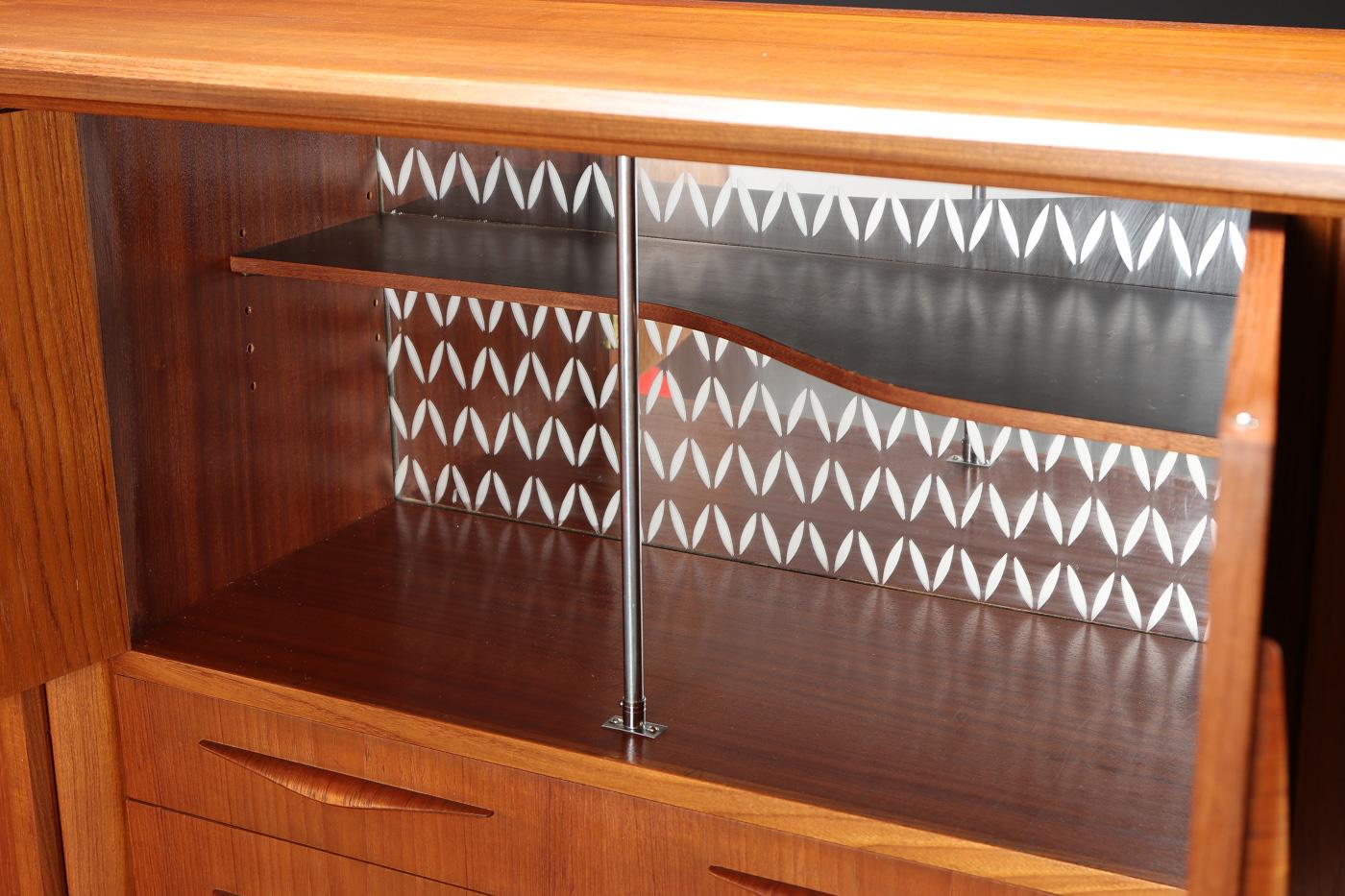 Danish modern teak sideboard by Danish furniture manufacturer. Sliding doors, drawers, and opening doors, with etched pattern mirrored glass inside.