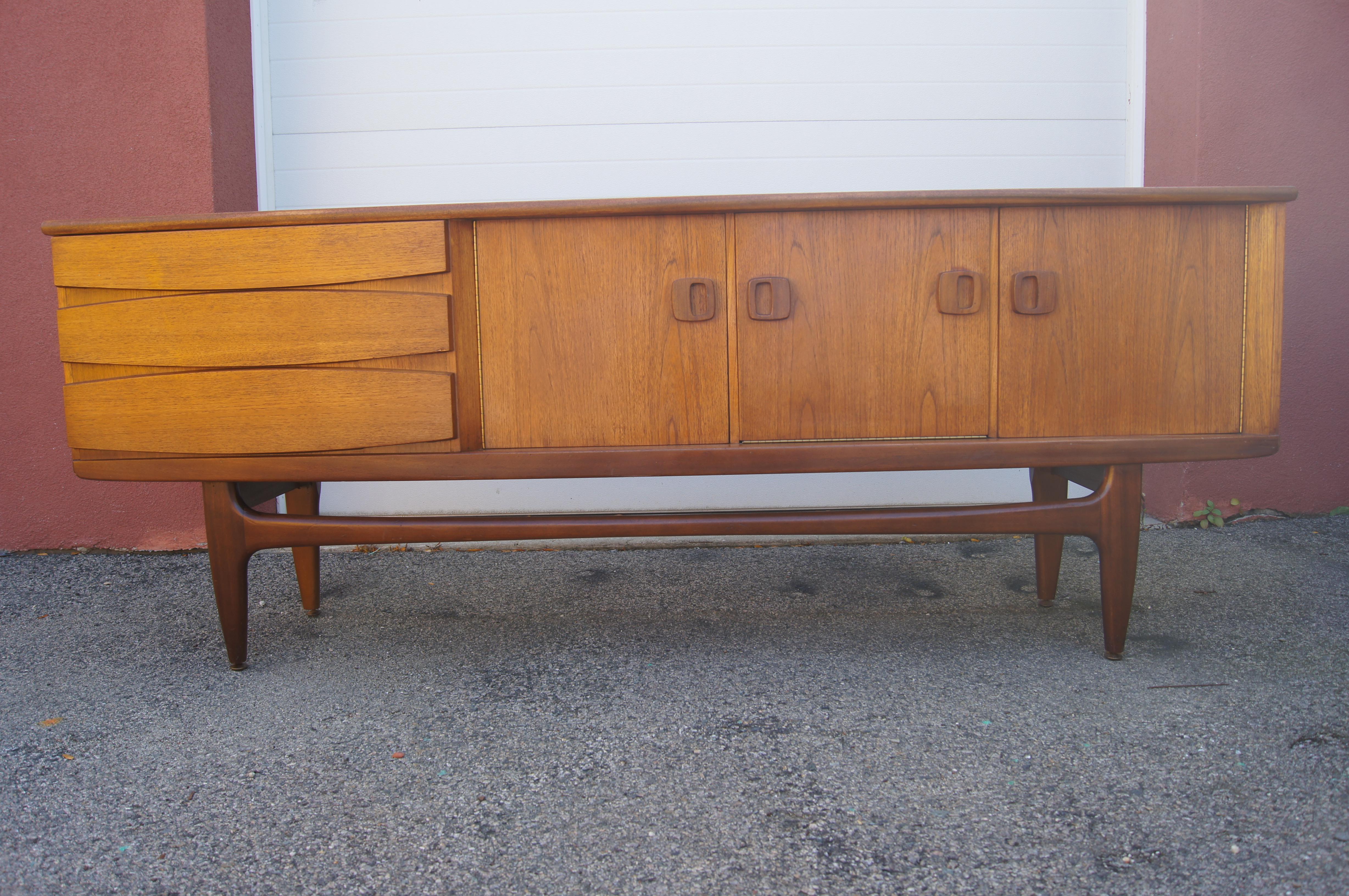 A beautiful example of Danish modernism, this wide teak sideboard features three drawers with shaped fronts and two doors that conceal adjustable shelving on either side of a drop-down door that hides white laminate shelving. The case sits on a