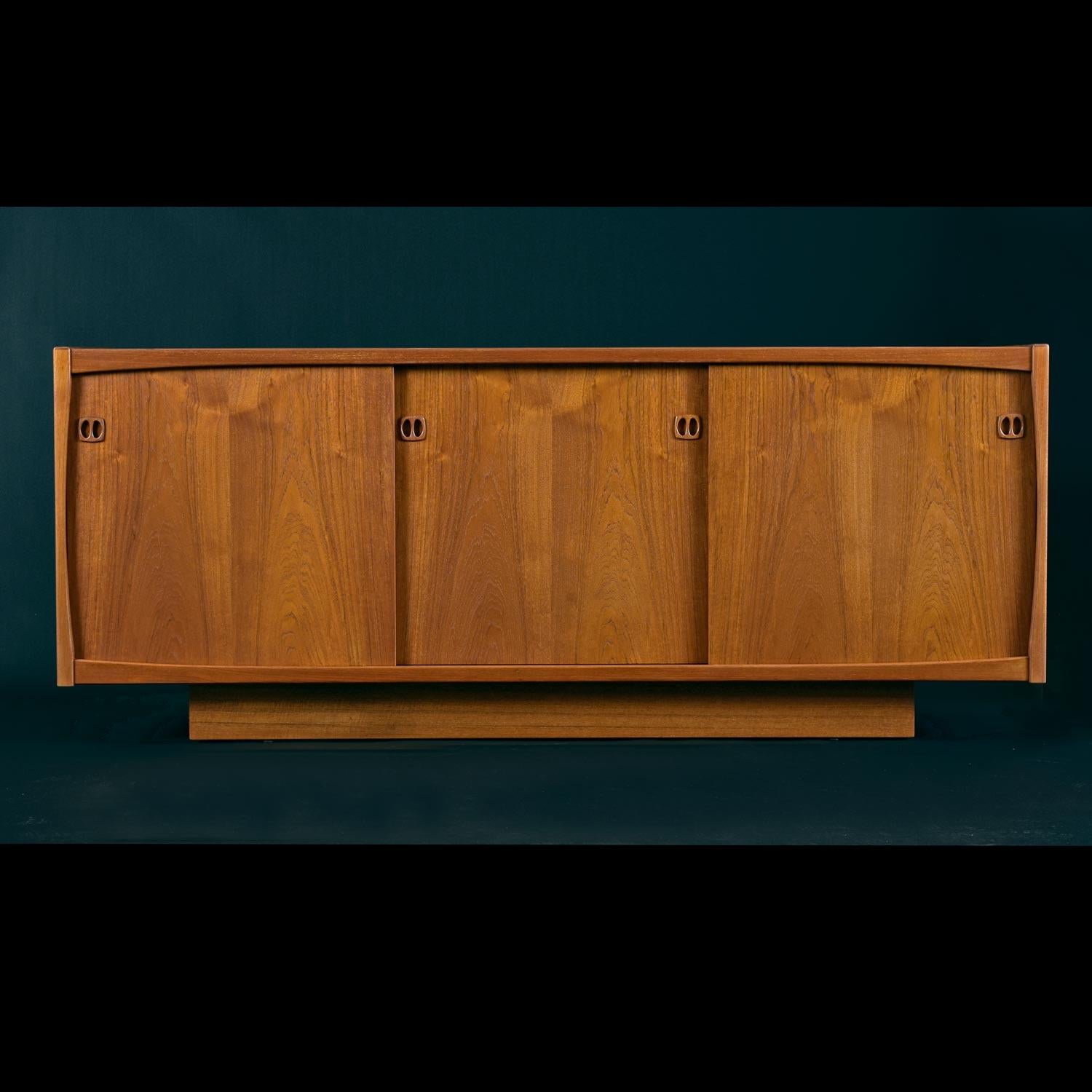 Vintage Danish Modern credenza by Laurits M Larsen. Ideal for use as a sideboard or entertainment center. Three sliding doors at front allow easy access to cabinet interior. Minimalist facade is accented by elegantly sculpted recessed teak pulls.