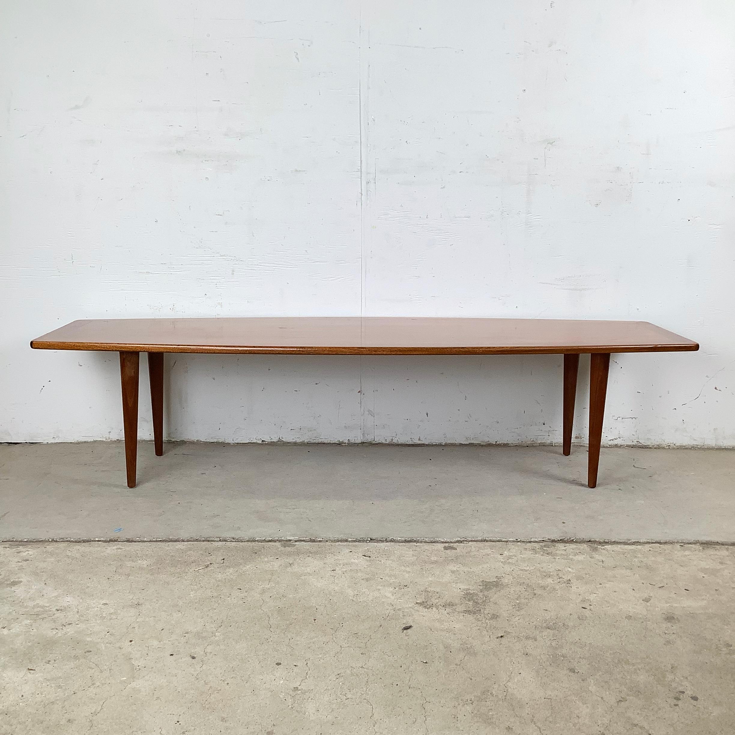 Dieser moderne Couchtisch aus dänischem Teakholz ist ein markantes Beispiel für das skandinavische Design der Mitte des Jahrhunderts. Er zeichnet sich durch seine lange, sanft gerundete Platte und die sich fein verjüngenden Beine aus. Die