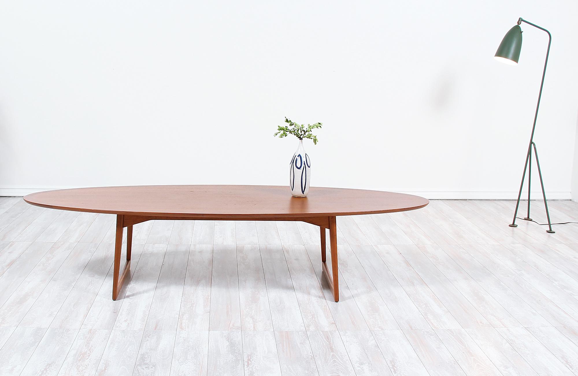 Elegant surfboard style coffee table imported from Denmark by Moreddi circa 1950s. This fantastic design has been meticulously crafted in teak wood and supported by a sled style and slightly angled sculptural legs. The tabletop shows a richly warm