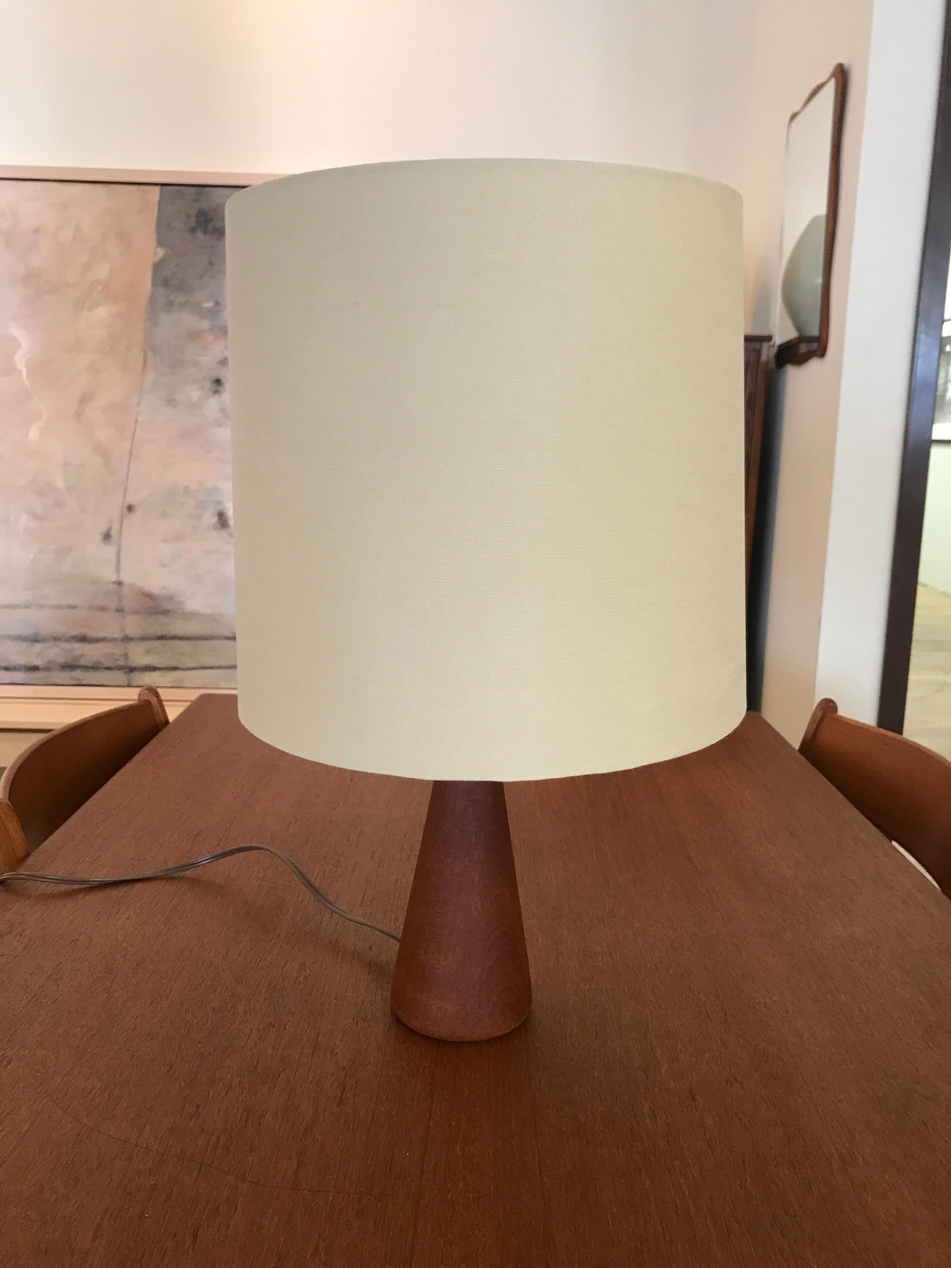 This table lamp made from old growth teak features an elongated spool shaped base with a lustrous oil finish and a new linen shade. A great accent piece that will add charm to any room.