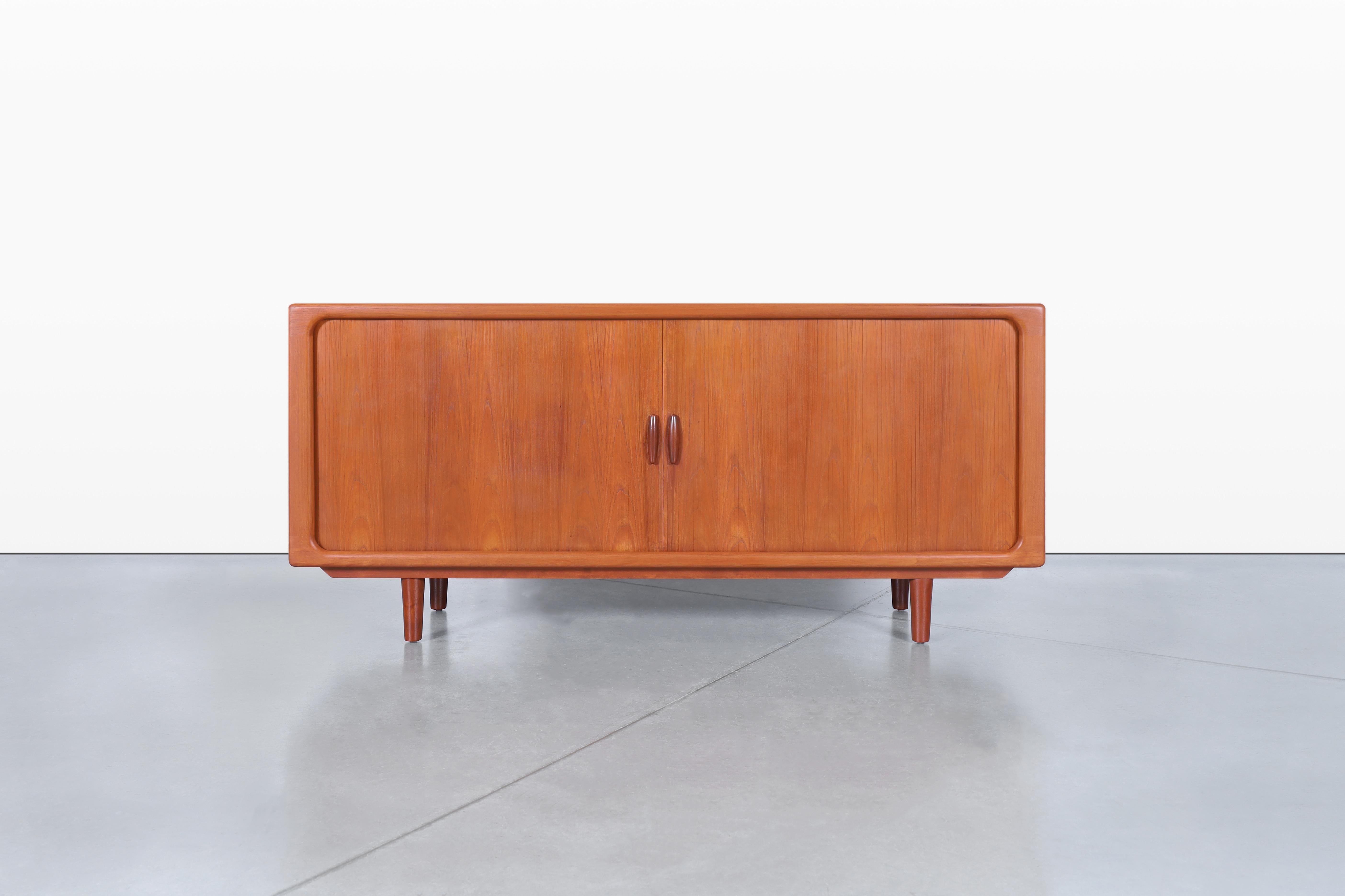 Este impresionante aparador moderno danés de teca, fabricado por Dyrlund en la década de 1970, es un verdadero testimonio de los principios del diseño escandinavo. Sus líneas elegantes y su cálida madera de teca aportan elegancia y funcionalidad a