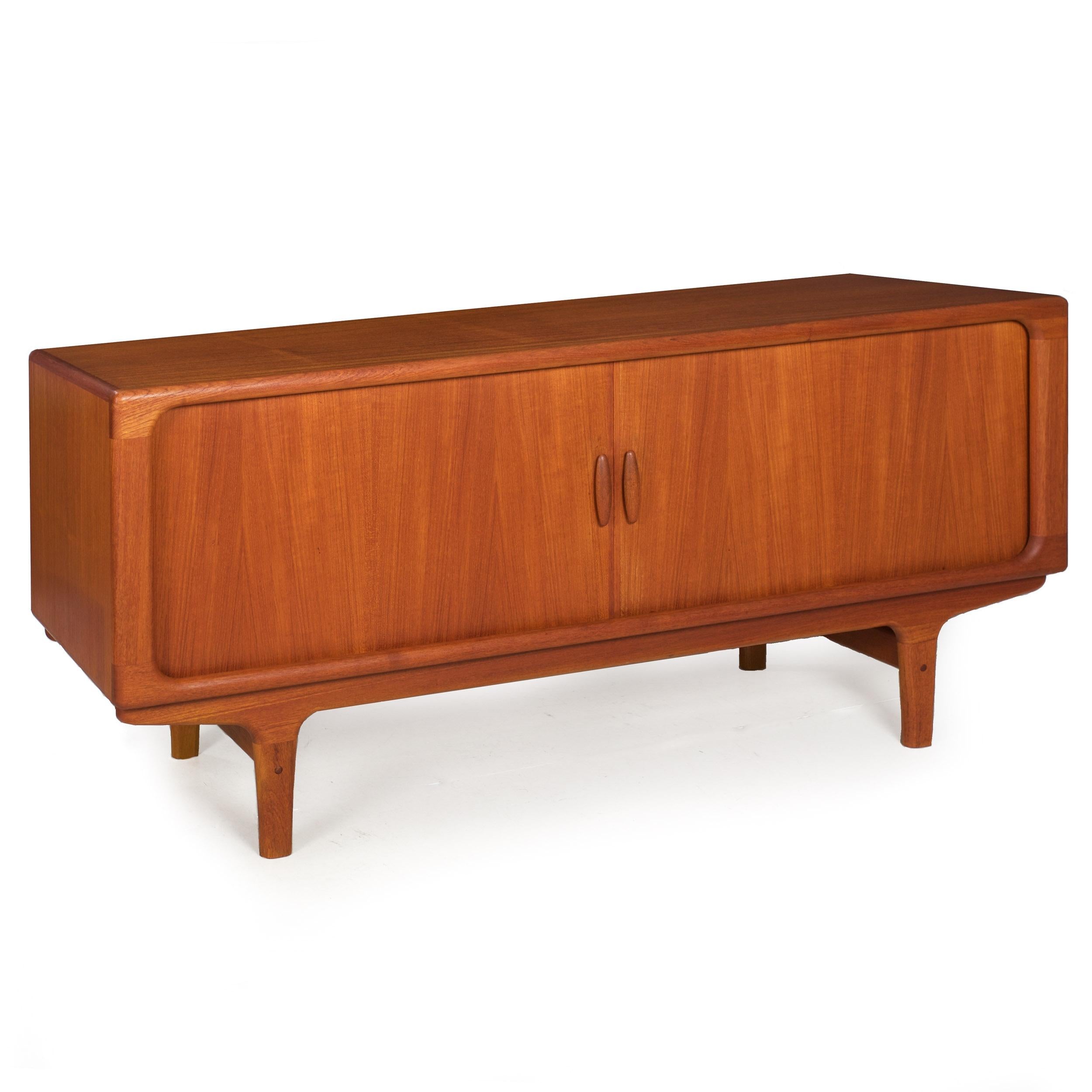 A very well-preserved low sideboard credenza designed and executed by Dryland of Denmark in the 1960s, it features an all-over teak surface with disappearing tambour doors that operate using sculpted solid teak handles to reveal a shelved interior