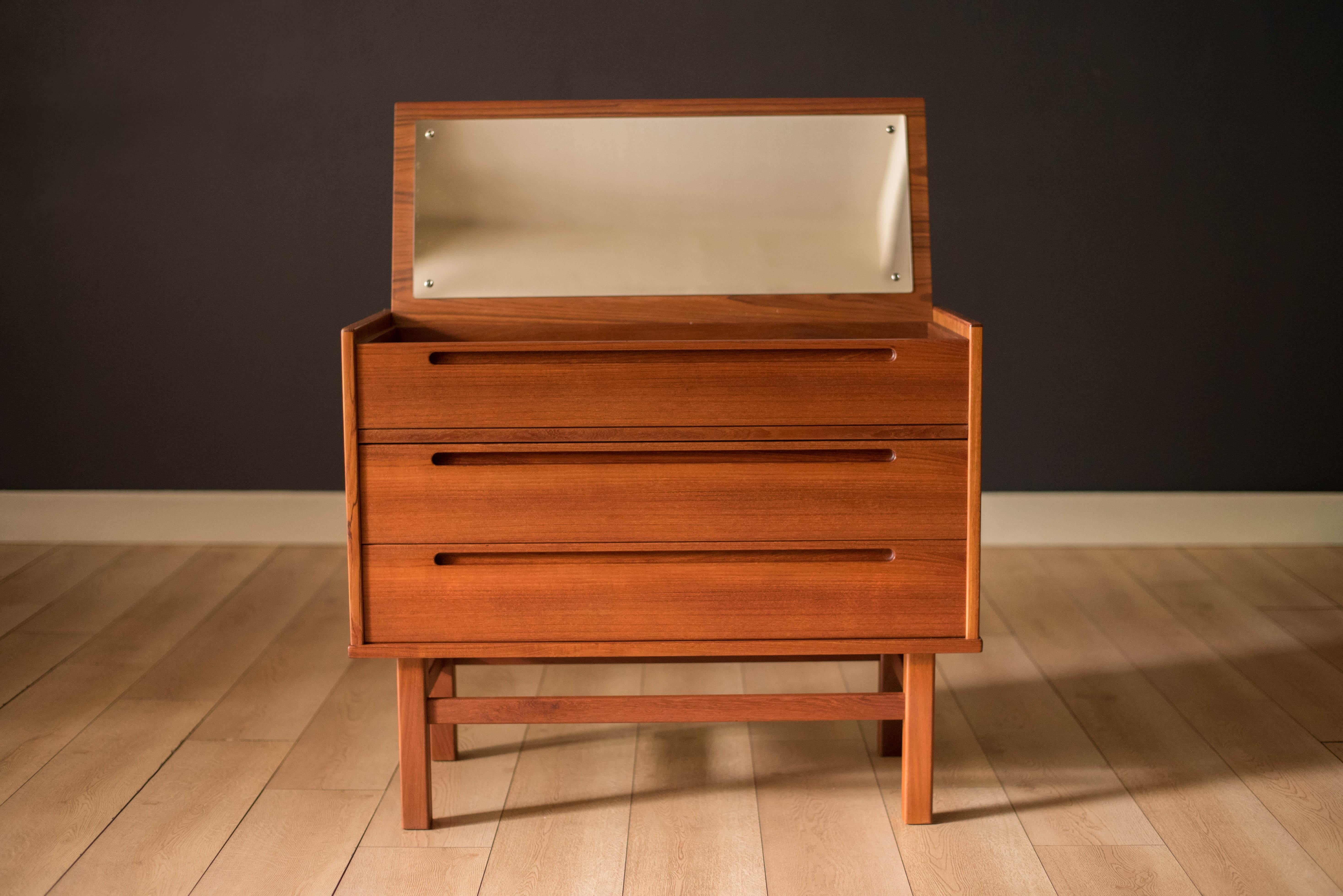 Mid-Century Modern dresser chest in teak designed by Nils Jonsson circa 1960s. Equipped with three storage drawers accessorized with sculpted inset pulls and dovetail construction. Features a hidden mirror vanity and a finished teak interior drawer