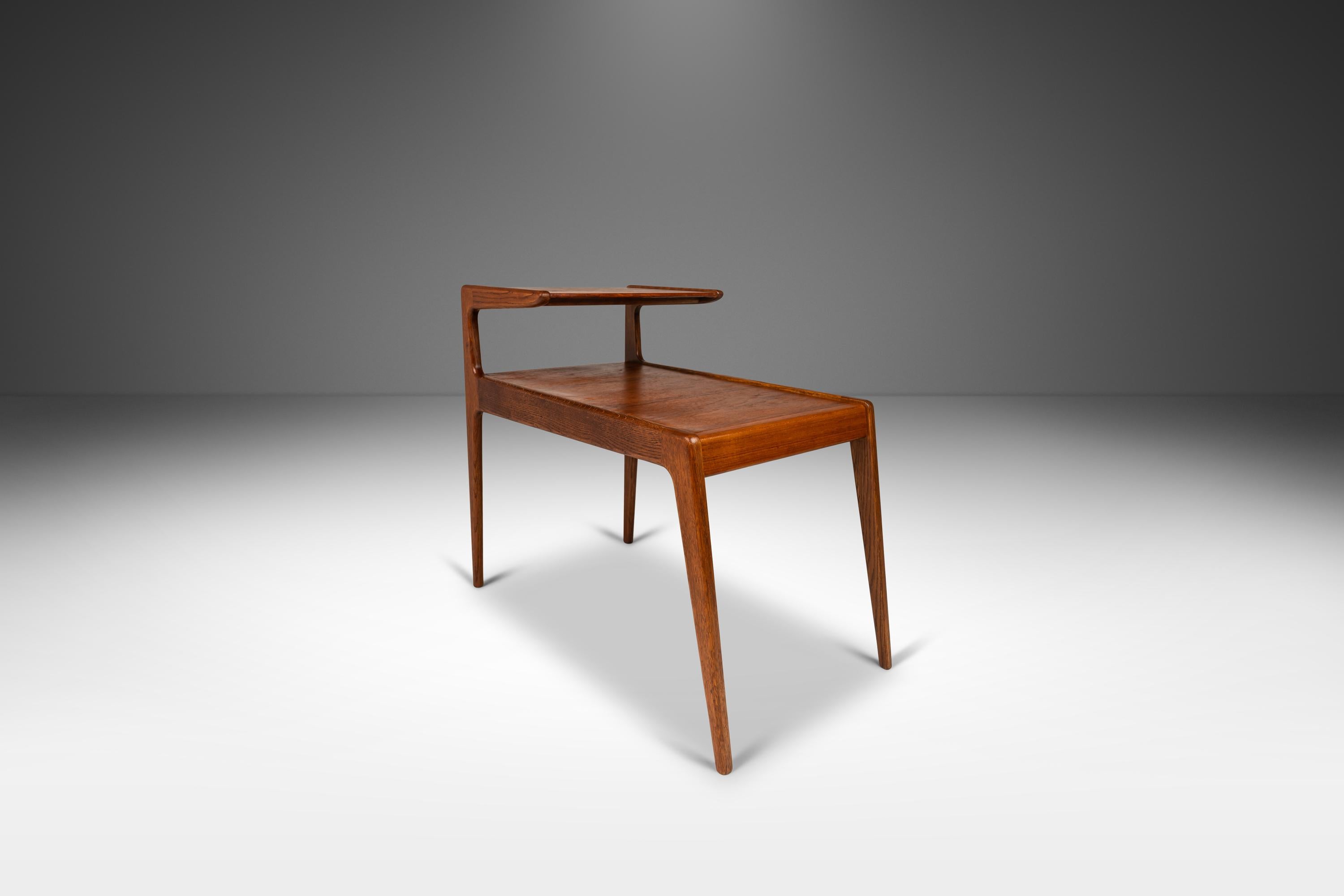 Introducing a rare and limited two-tier side table in teak by Kurt Østervig for Jason Møbler, crafted in the 1960's in Denmark. This now iconic table is constructed from a mix of solid and veneered Burmese teak, showcasing the natural beauty of the
