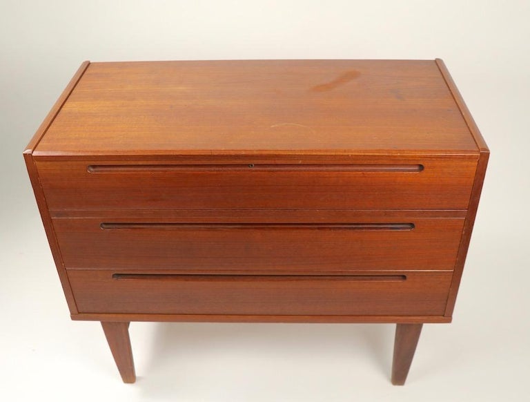 Interesting midcentury Danish modern flip top chest of drawers, having a flip up top surface which opens to reveal divided storage spaces, over three deep storage drawers. Selling in original condition, the top surface has a significant scratch,