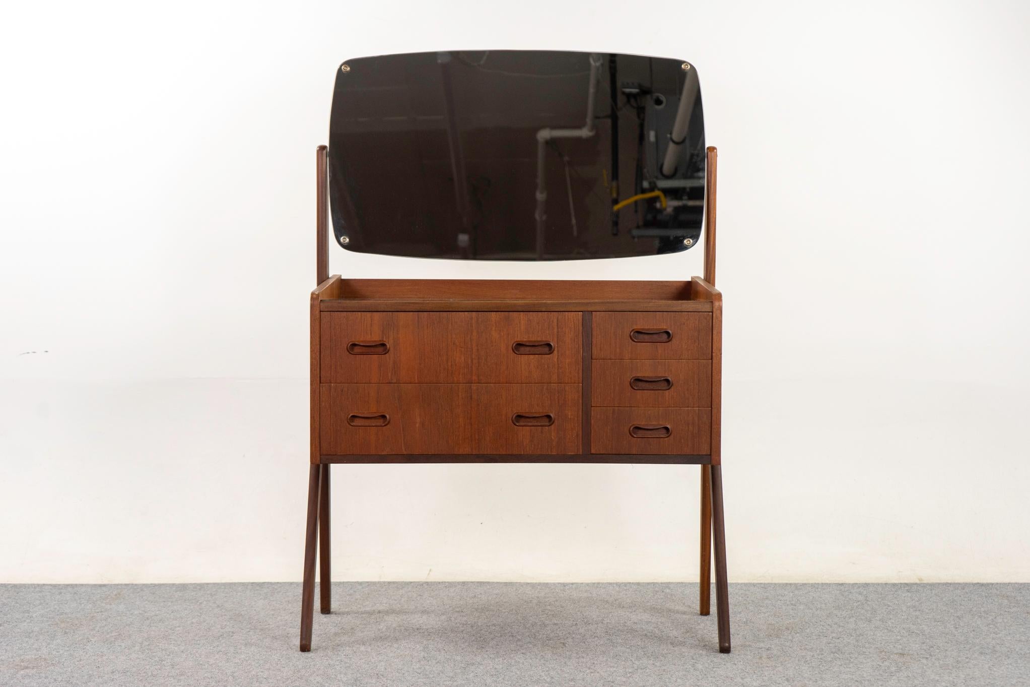Teak Danish vanity, circa 1960's. Solid wood trim and stunning bookmatched veneer. Dramatic scissor legs and original swivel mirror. Atomic patterned glass top with some minor wear and tear. Stunning silhouette!   

Unrestored item with option to