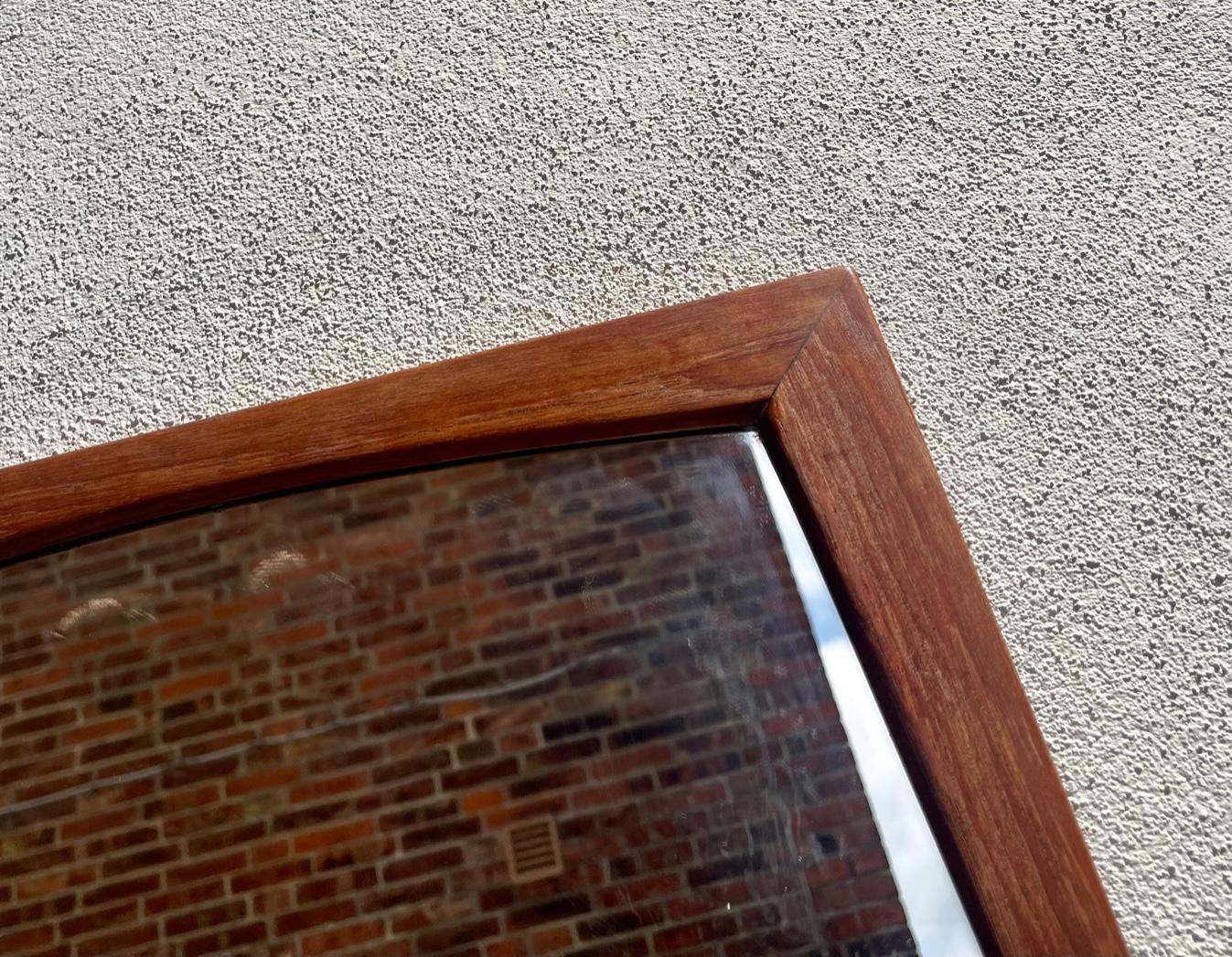 A wall hung mirror with solid and slightly concave teak profiles that has been assembled without the use of metal. It was manufactured and designed by Aksel Kjersgaard in Denmark during the 1960s. Design number: 105. Measurements: H: 104 cm, W: 43