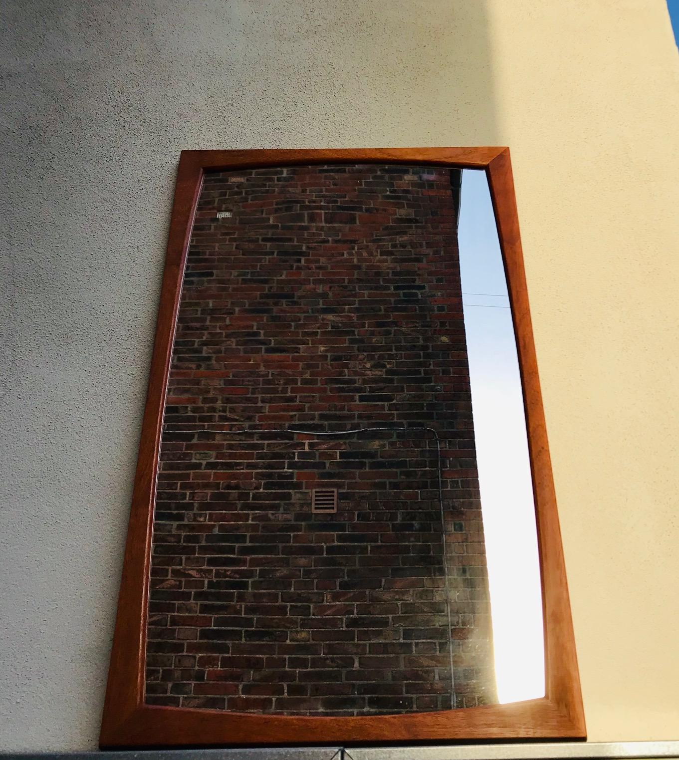 A wall-hung mirror with solid and slightly concave teak profiles that has been assembled without the use of metal. It was manufactured by Aksel Kjersgaard in Denmark during the 1960s.