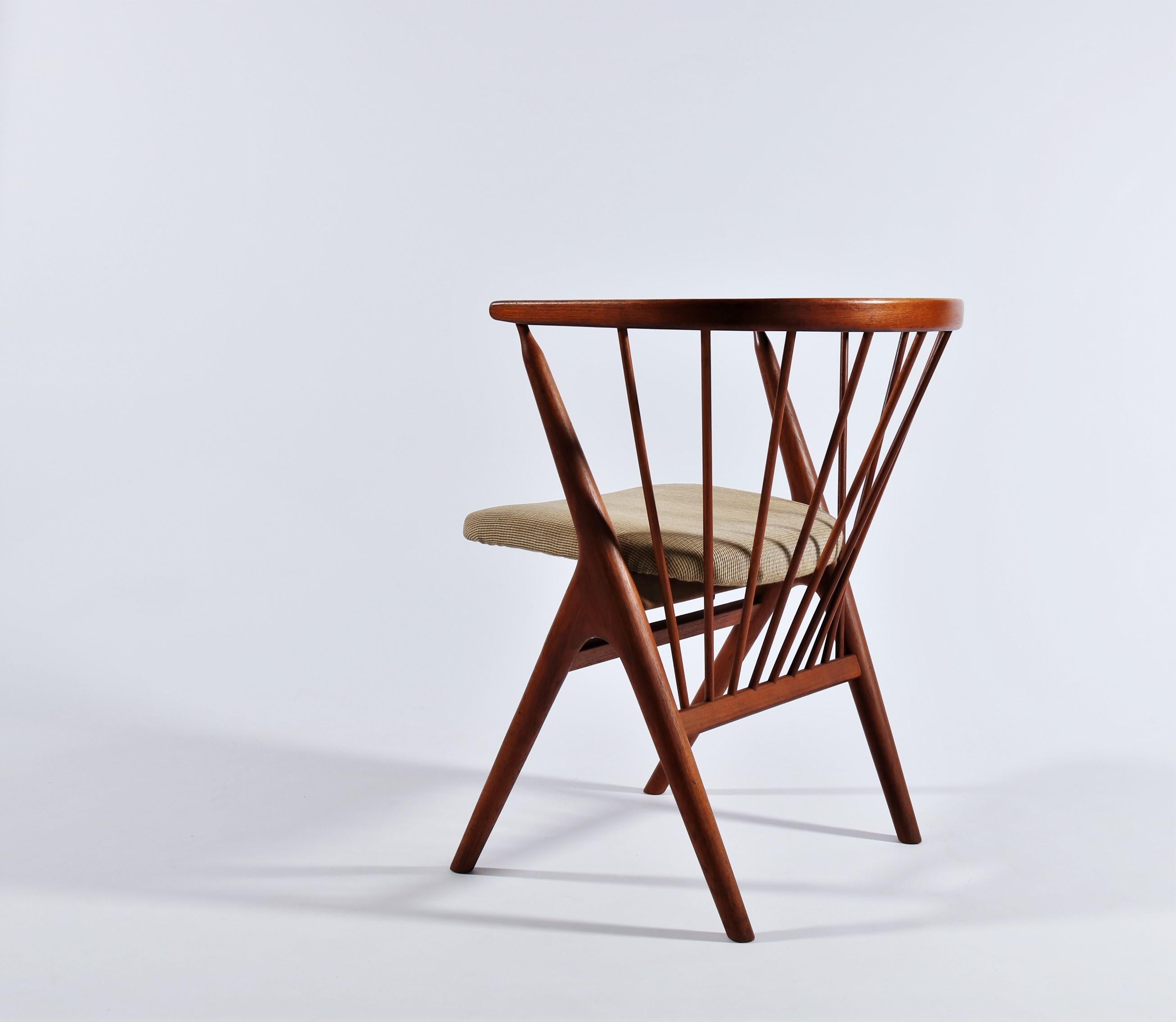 Iconic Danish Modern armchair in beautifully grained teak wood by Architect and Cabinetmaker Helge Sibast. The chair features a wonderfully patinated teak frame with scissor legs and spindled back. The seat is upholstered in high quality wool. This