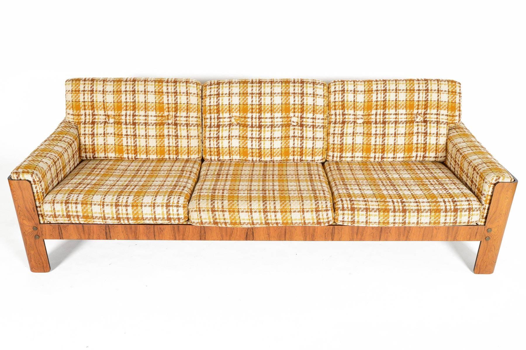 This Danish modern midcentury three-seat sofa hails from the early 1970s and is an exceptional find. The perfectly patinated rosewood frame holds the eight removable cushions and upholstered back. Brass hardware adds a finishing touch. This sofa