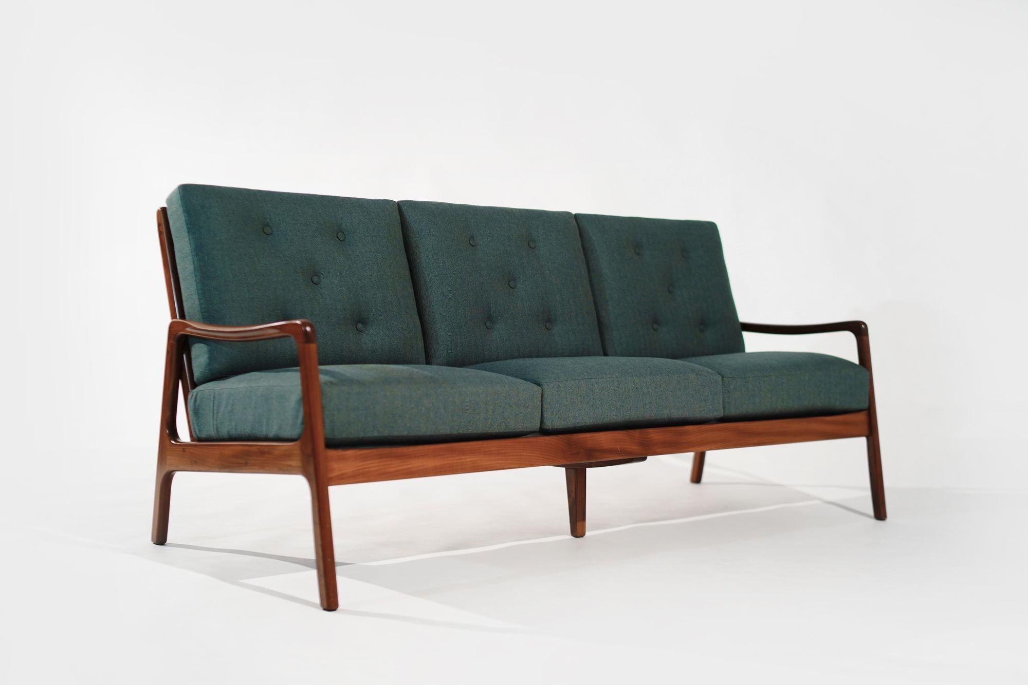 A Danish Modern three-seat sofa. Crafted in the 1960s, its teak frame has been fully restored, complemented by new cushions upholstered in a stylish green/teal linen.
This exquisite sofa will add a touch of vintage sophistication to your living