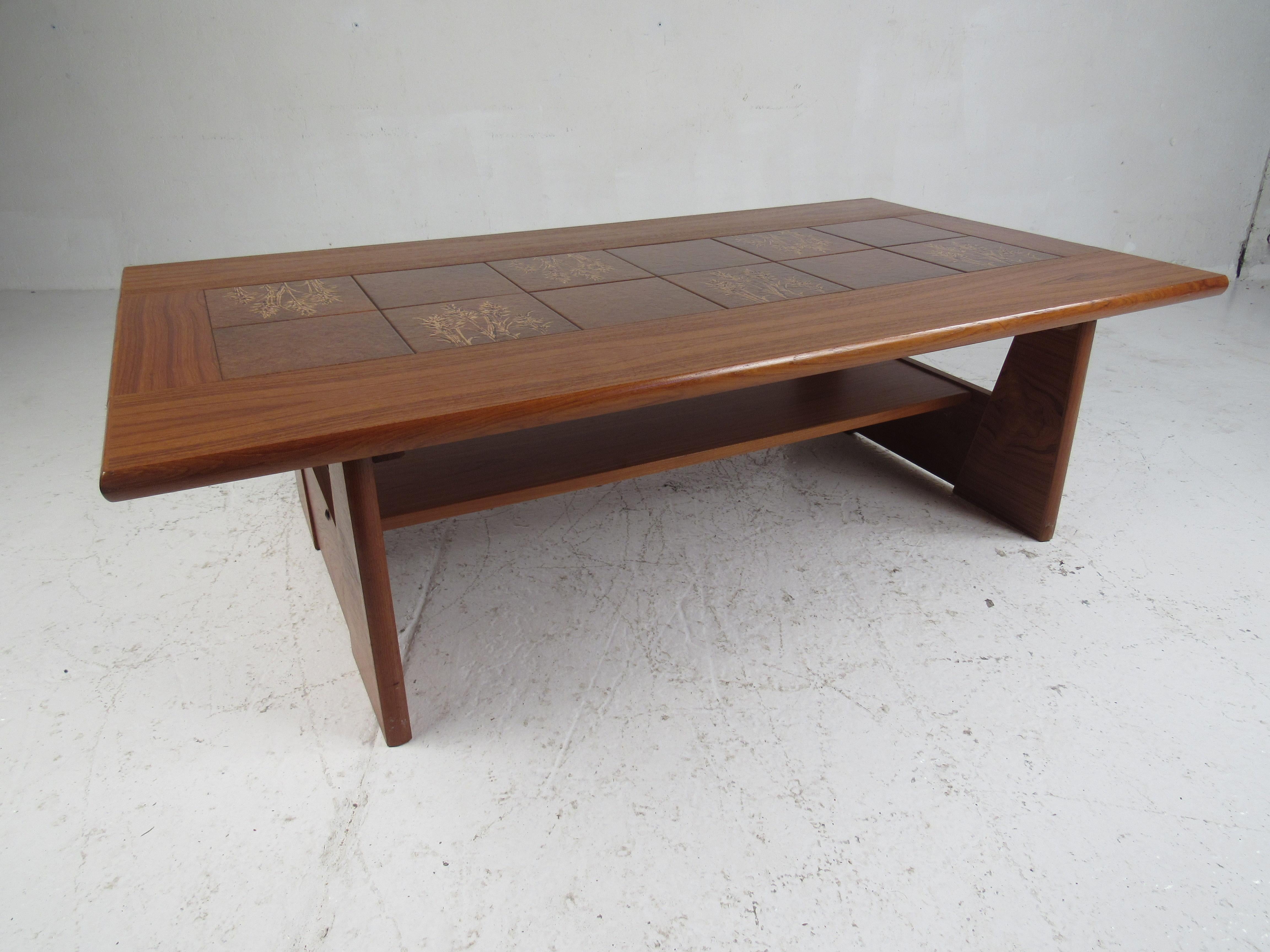 An elegant Mid-Century Modern coffee table with a tile top and elegant teak wood grain. This Gangsø Møbler style coffee table boasts unusual sled style legs with a stretcher running all the way across. Wonderful designs on the tile and a rich teak