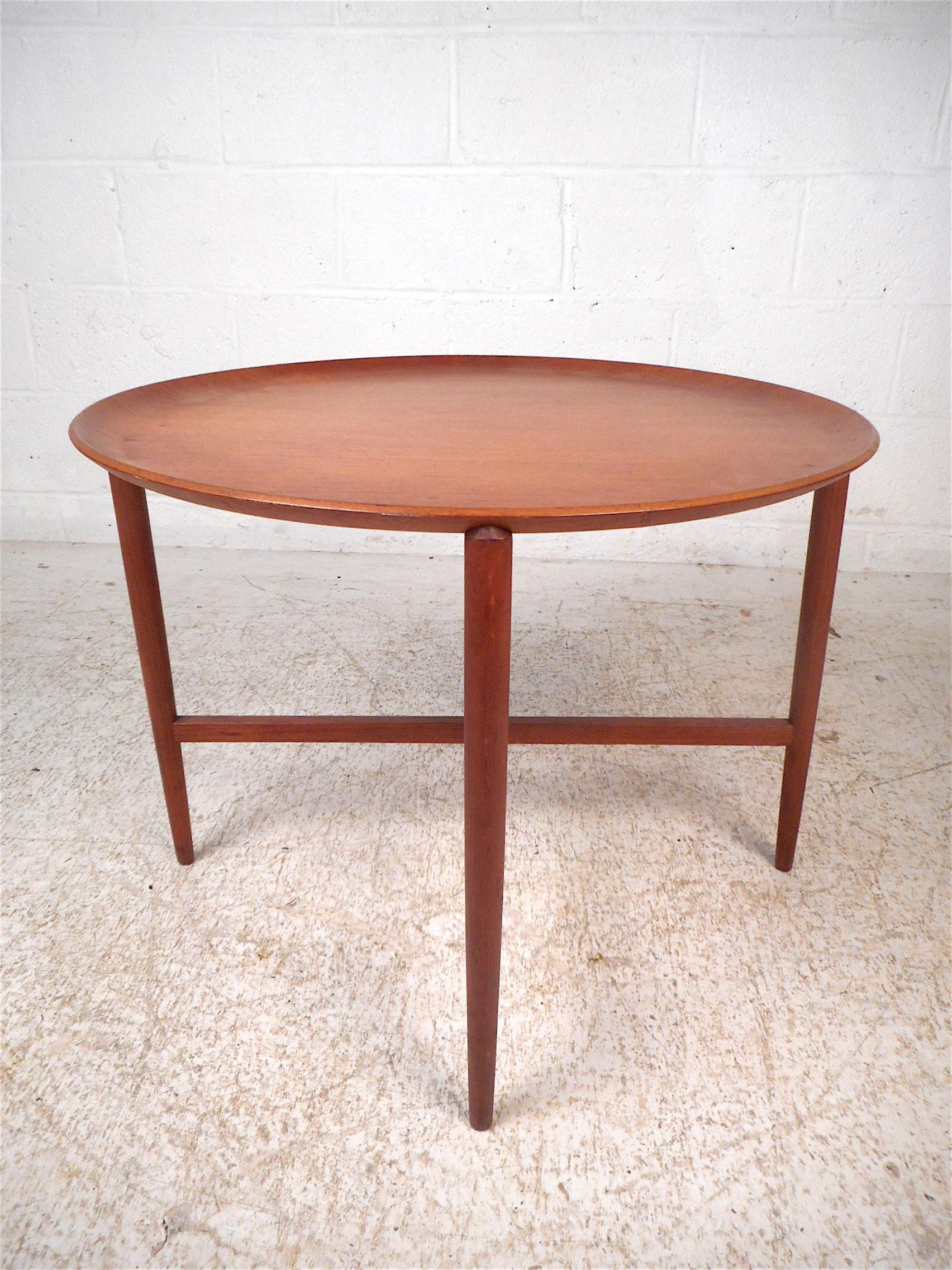 Stylish Danish modern tray table. Teak wood construction. The base's slim and sleek angular profile is complimented by the circular tabletop with raised edges. A nice piece sure to impress in any modern interior. Please confirm item location with
