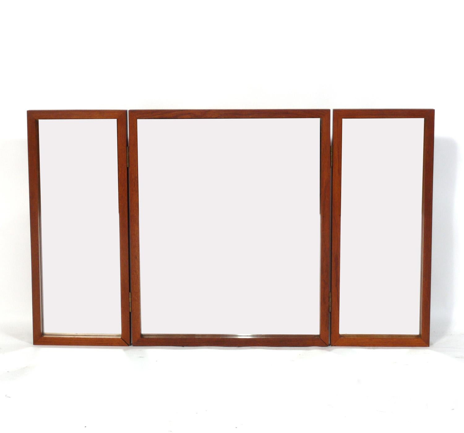 Danish Modern teak tri fold mirror, designed by Aksel Kjersgaard, Denmark, circa 1960s. Three panels are connected with hinges and can be rested on top a table or dresser, or mounted on the wall with the key-hole hangers in the back. The teak has