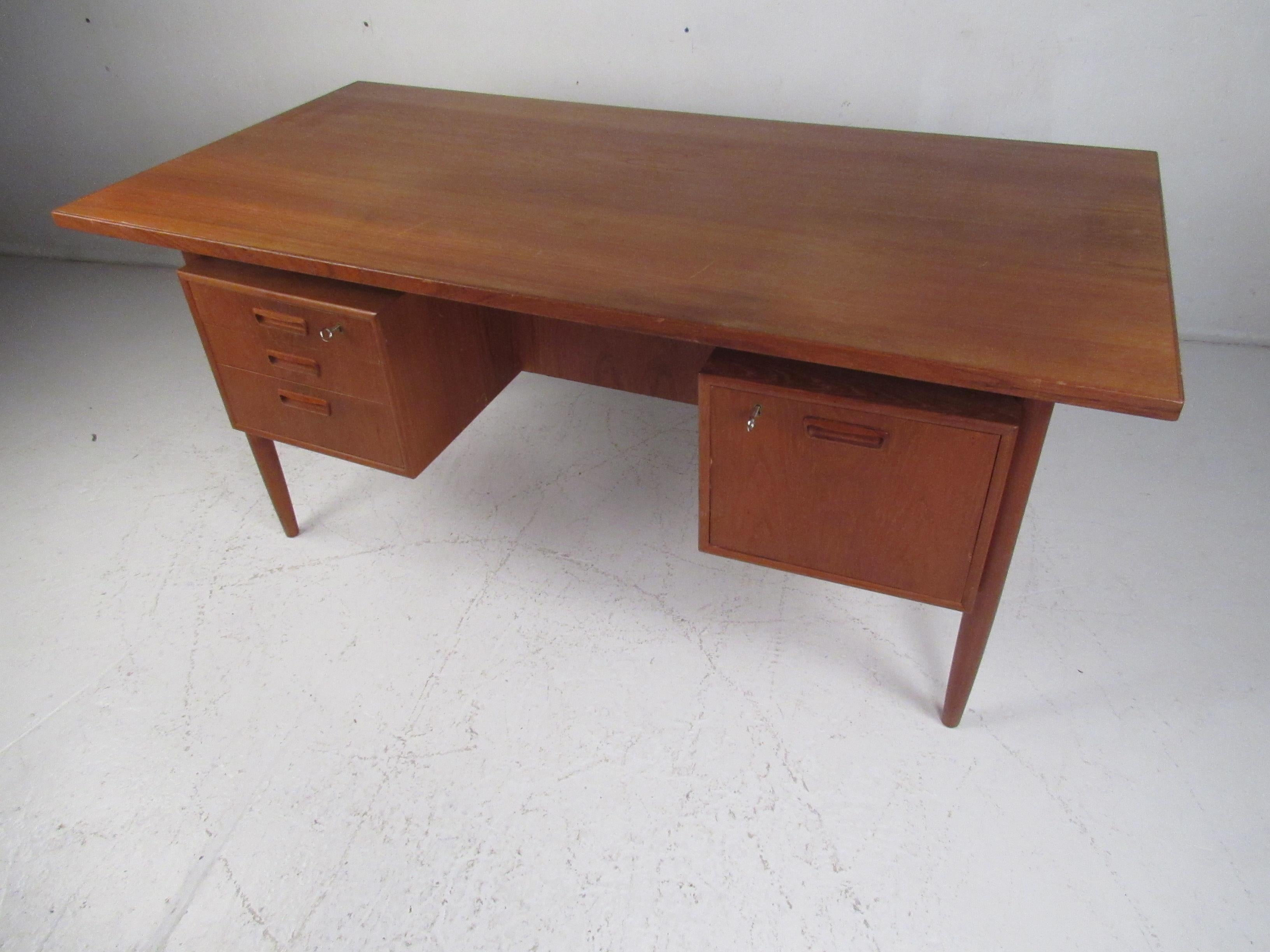 This sleek Mid-Century Modern desk features a twin pedestal base and a floating style top. A well-made Danish design that boasts four dovetailed drawers and a large tabletop ensuring plenty of work space. The carved drawer pulls, tapered legs, and