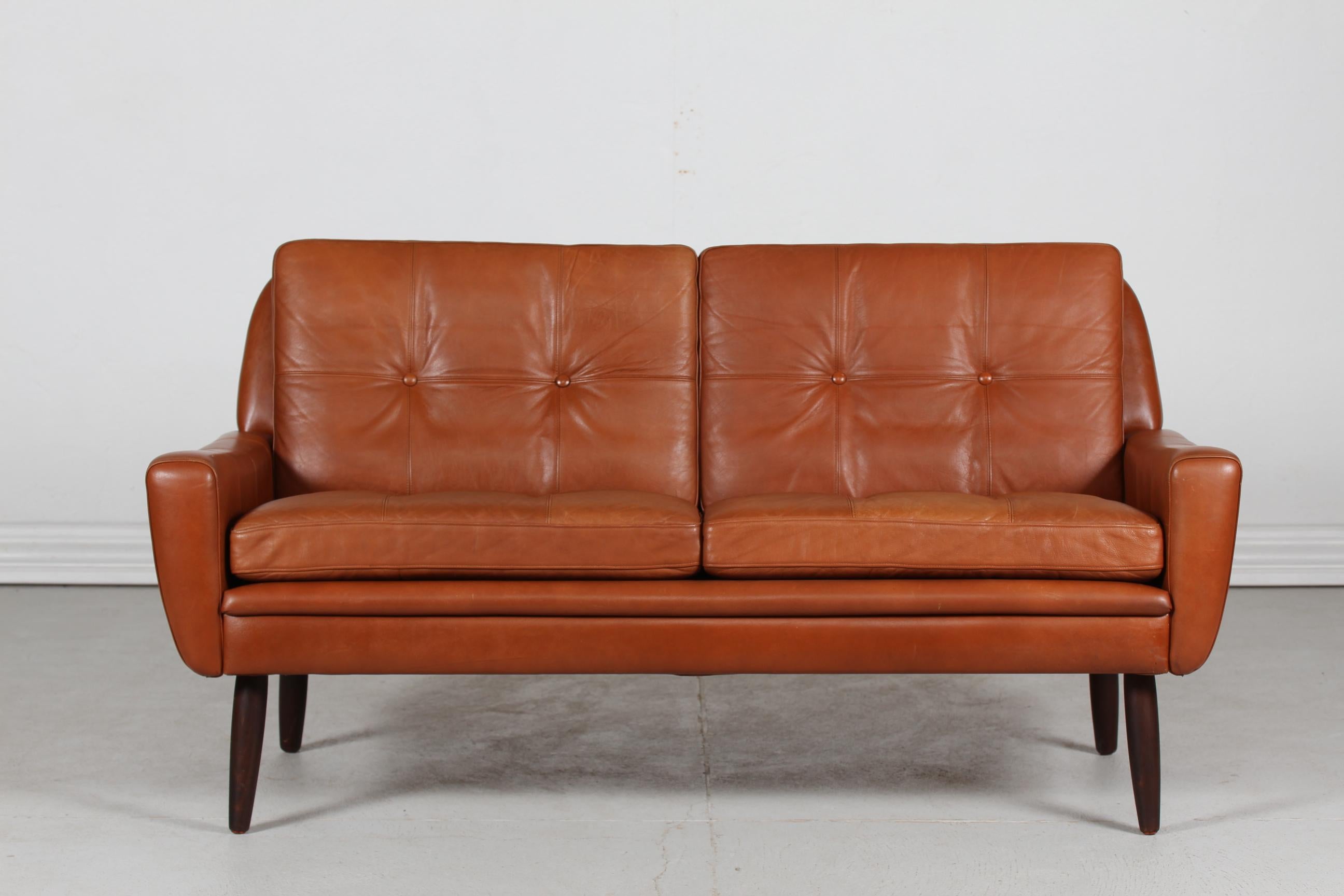 Danish vintage 2 seater sofa manufactured in Denmark in the 1960s.
It's upholstered with the original cognac-colored leather with light patina, leather buttons and removable cushions
The slightly conical legs are made of dark stained wood.

This