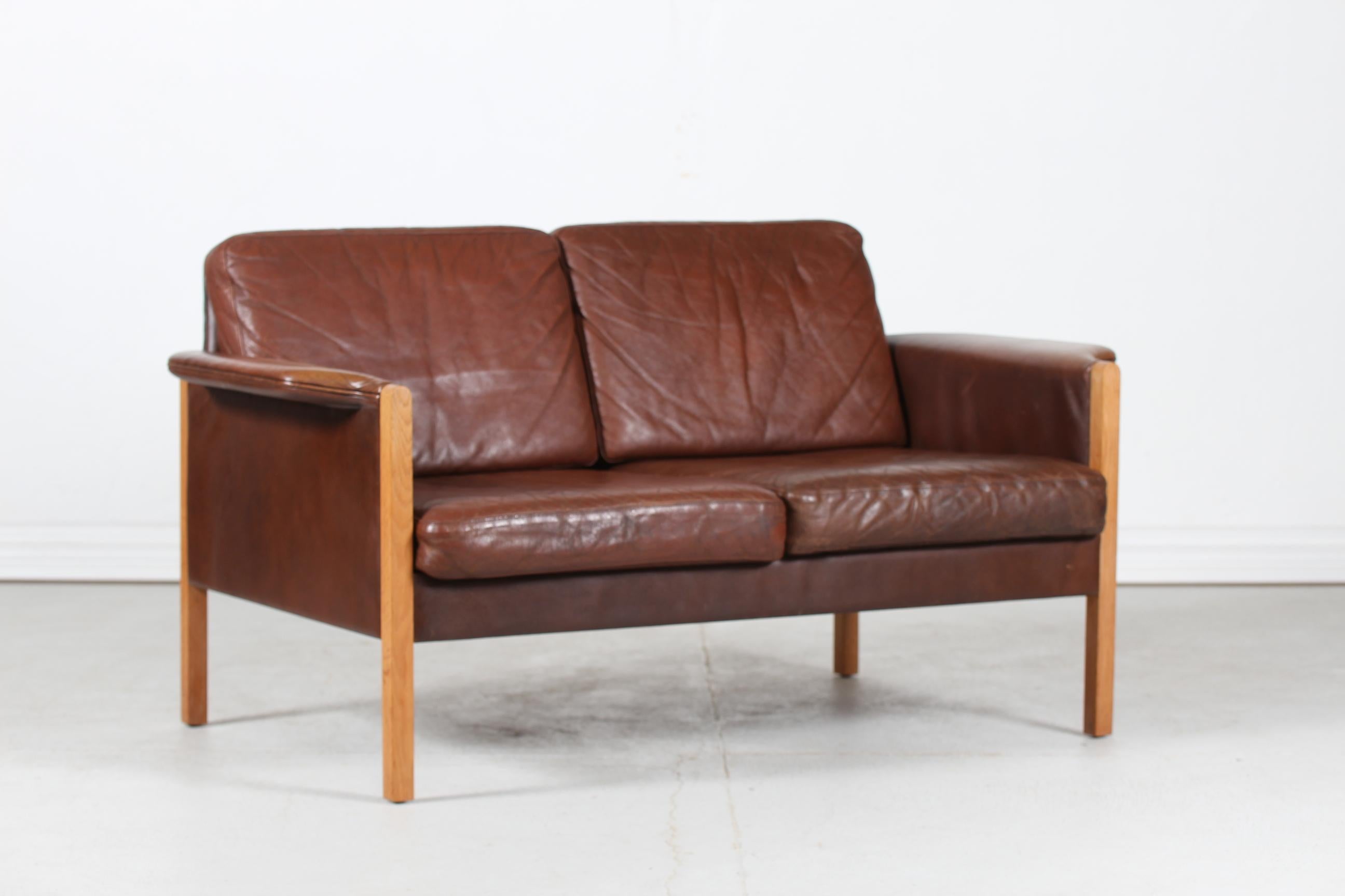 Danish vintage sofa for 2 persons in the style of Finn Juhl manufactured in Denmark in the 1970s.
It's upholstered with the original dark cognac-colored leather/almost brown with light patina after use and age. 
The legs and frame are made of