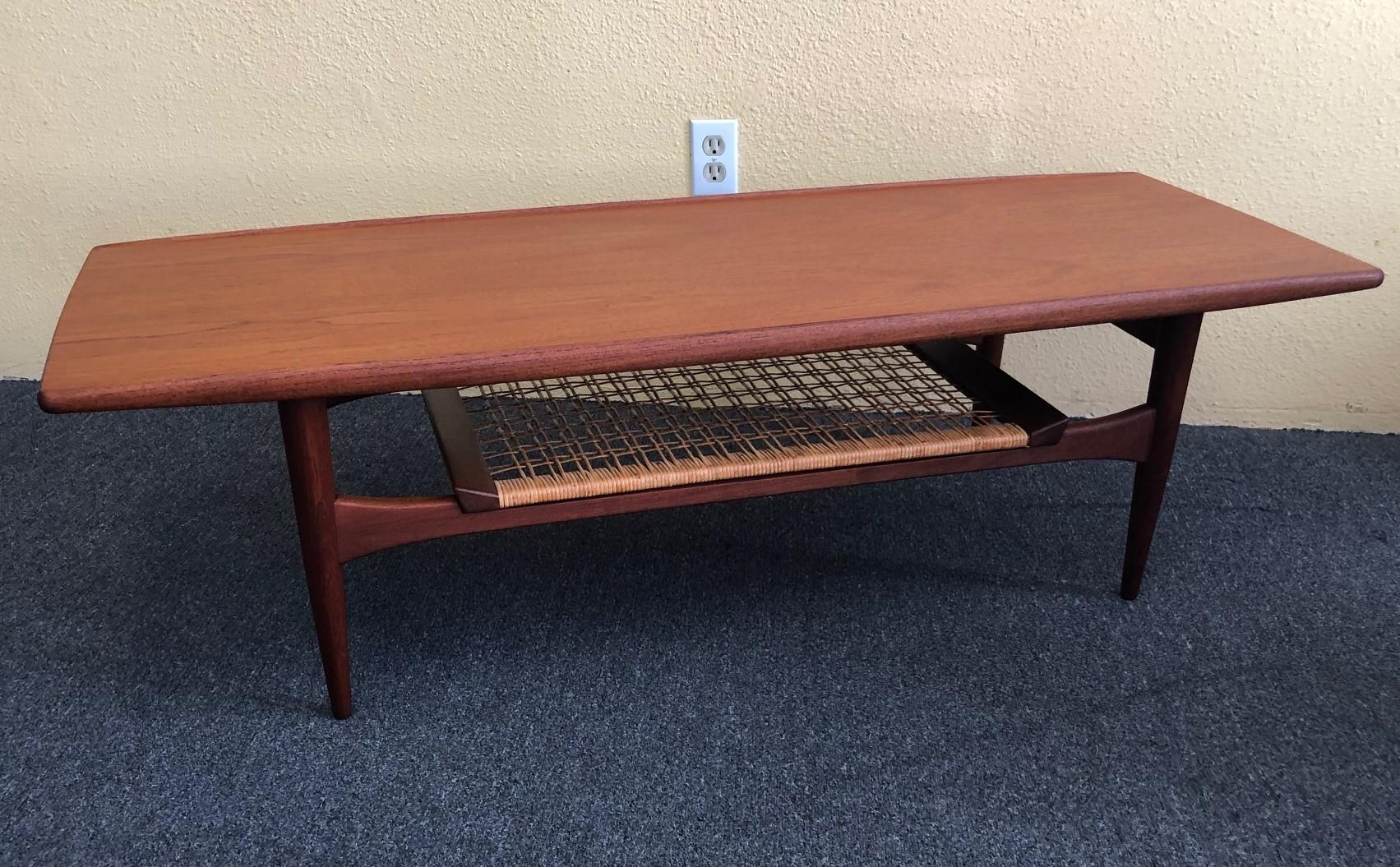 Stunning Danish modern two-tier, surfboard style teak coffee table attributed to Hans Wegner by Moreddi, circa 1960's. Features include a turned edge running the width of the table and a lower level caned shelf which has an interesting raised edge.