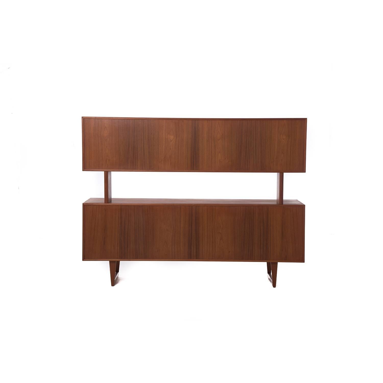 This Kurt Ostervig teak sideboard with sleigh legs features lower storage with a series of drawers and doors and a detachable upper shelving component with sliding glass doors.