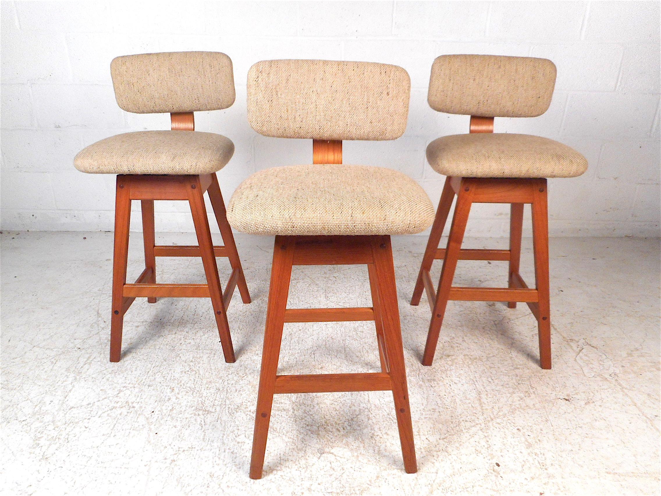 Impressive set of 3 Danish modern stools. Sleek angular Teak wood frame, swiveling seats and backrests covered in a vintage beige upholstery. Stylish and comfortable, these Danish stools are sure to impress in any modern interior. Please confirm