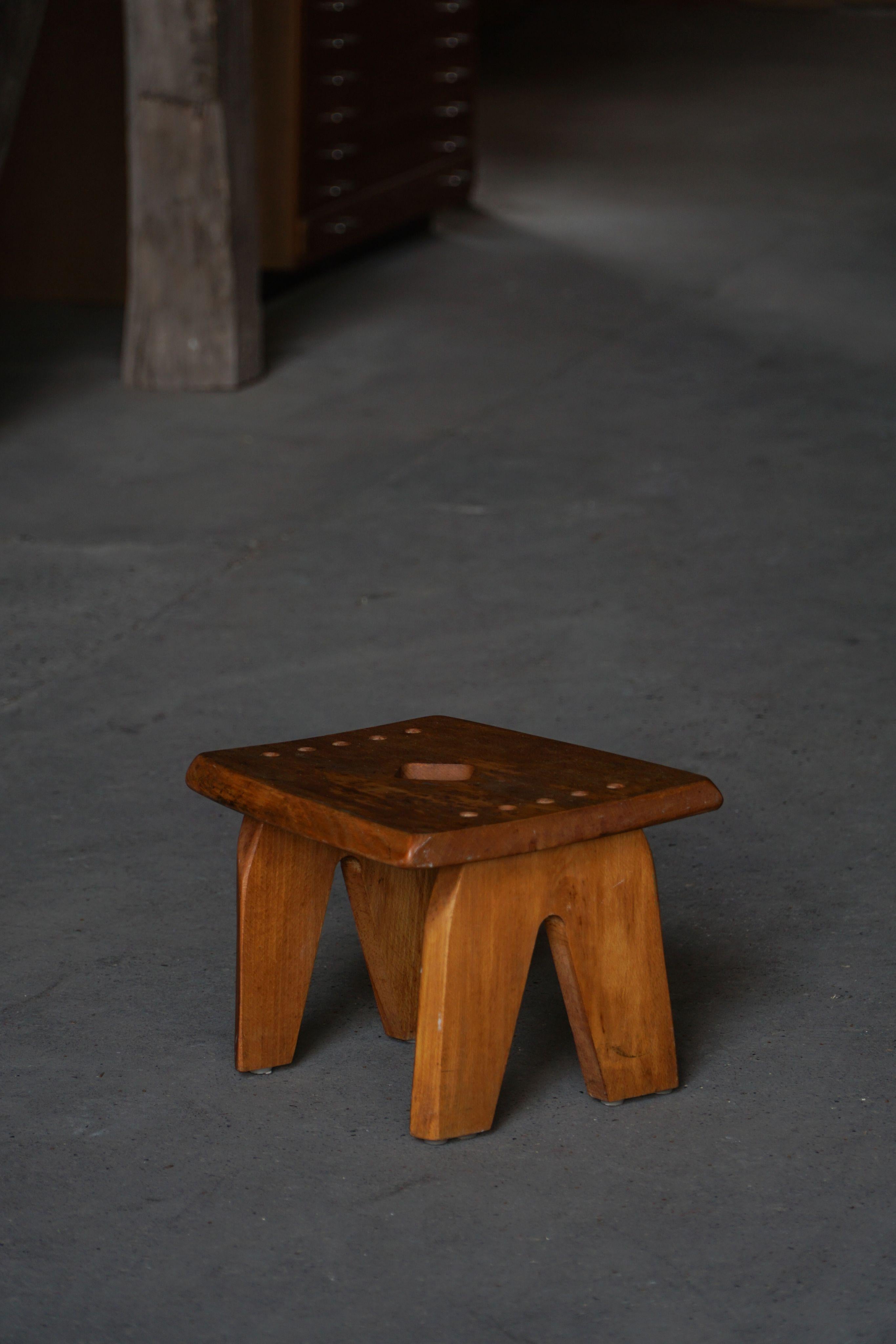 Un encantador y decorativo taburete escandinavo de olmo macizo, fabricado a mano por un ebanista danés en la década de 1960. Esta pieza refleja la elegancia rústica del diseño popular nórdico, con su construcción robusta, su tono cálido y su pátina
