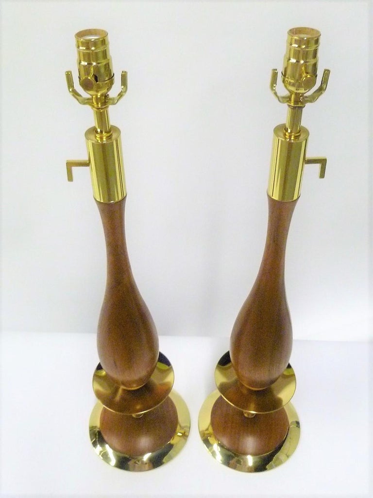 Absolutely stellar pair of figured walnut and luxe brass table lamps in a stylized candlestick form, 1950s Mid-Century Modern design, in the style of Tony Paul, with refinished walnut and professionally polished and lacquered heavy brass elements.