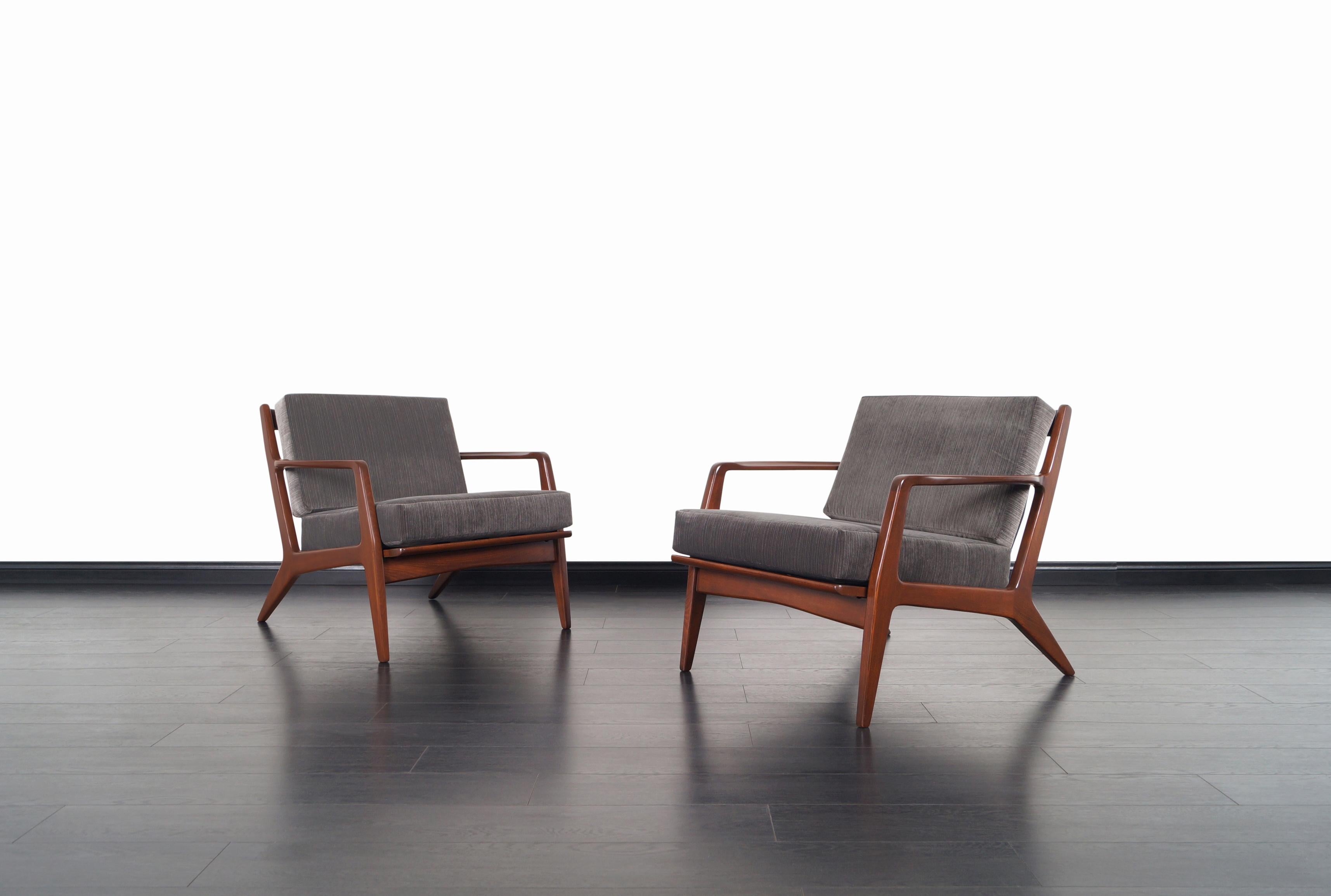 An amazing pair of Danish modern walnut lounge chairs designed by architect and furniture designer Ib Kofod-Larsen for Selig in Denmark, circa 1960s. These elegant ergonomic lounge chairs feature a solid walnut stained beech frame with angled legs