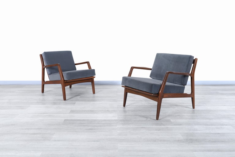 Exceptional Danish modern walnut lounge chairs designed by the iconic Danish designer Ib Kofod-Larsen for Seling in Denmark, circa 1960s. Each chair features a solid walnut frame with angled legs and sculpted slatted backrest, assuring a sleek