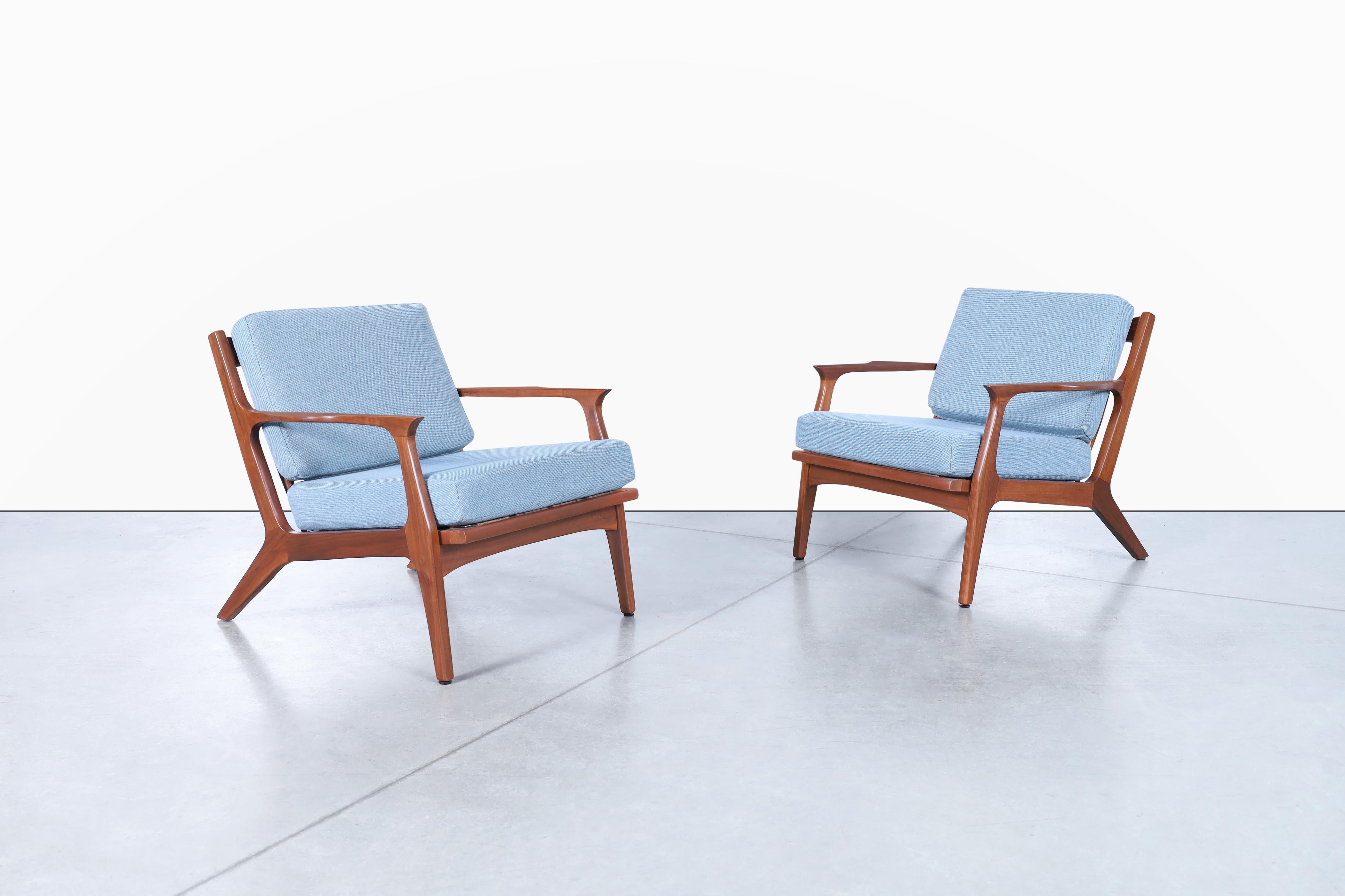 Stunning Danish modern walnut lounge chairs inspired by the iconic Danish designer Ib Kofod-Larsen for Selig in Denmark, circa 1960s. These chairs are truly stunning! The solid walnut frame is expertly crafted to create a sleek and elegant profile