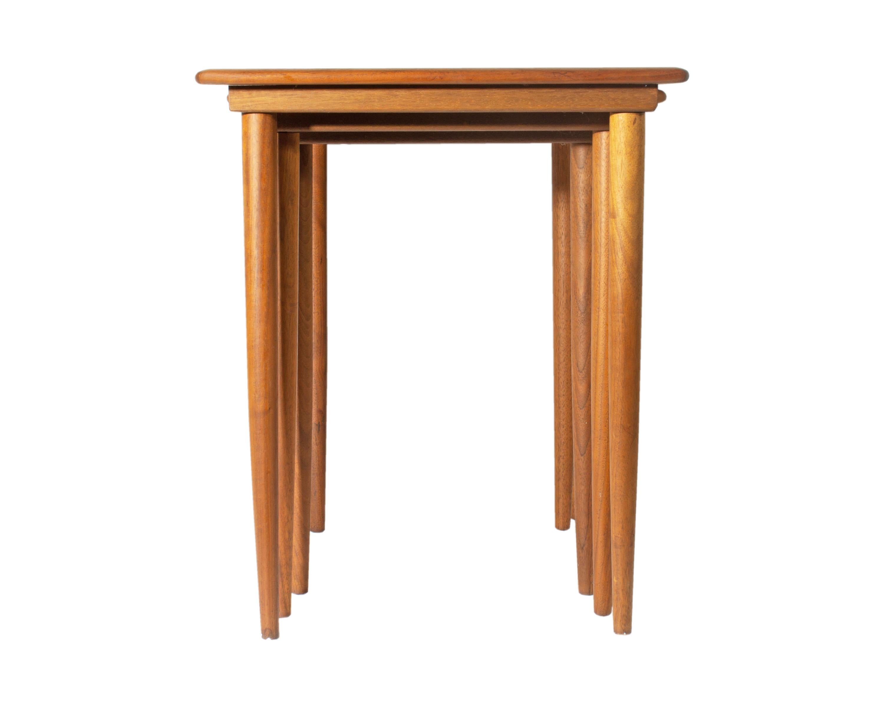 A set of rectangular Danish Modern nesting tables. Made in Denmark, these three tables feature a slim profile and are made of walnut. Each of the tables features a two-tone top and tapered legs. The table slides into a groove which secures it to the