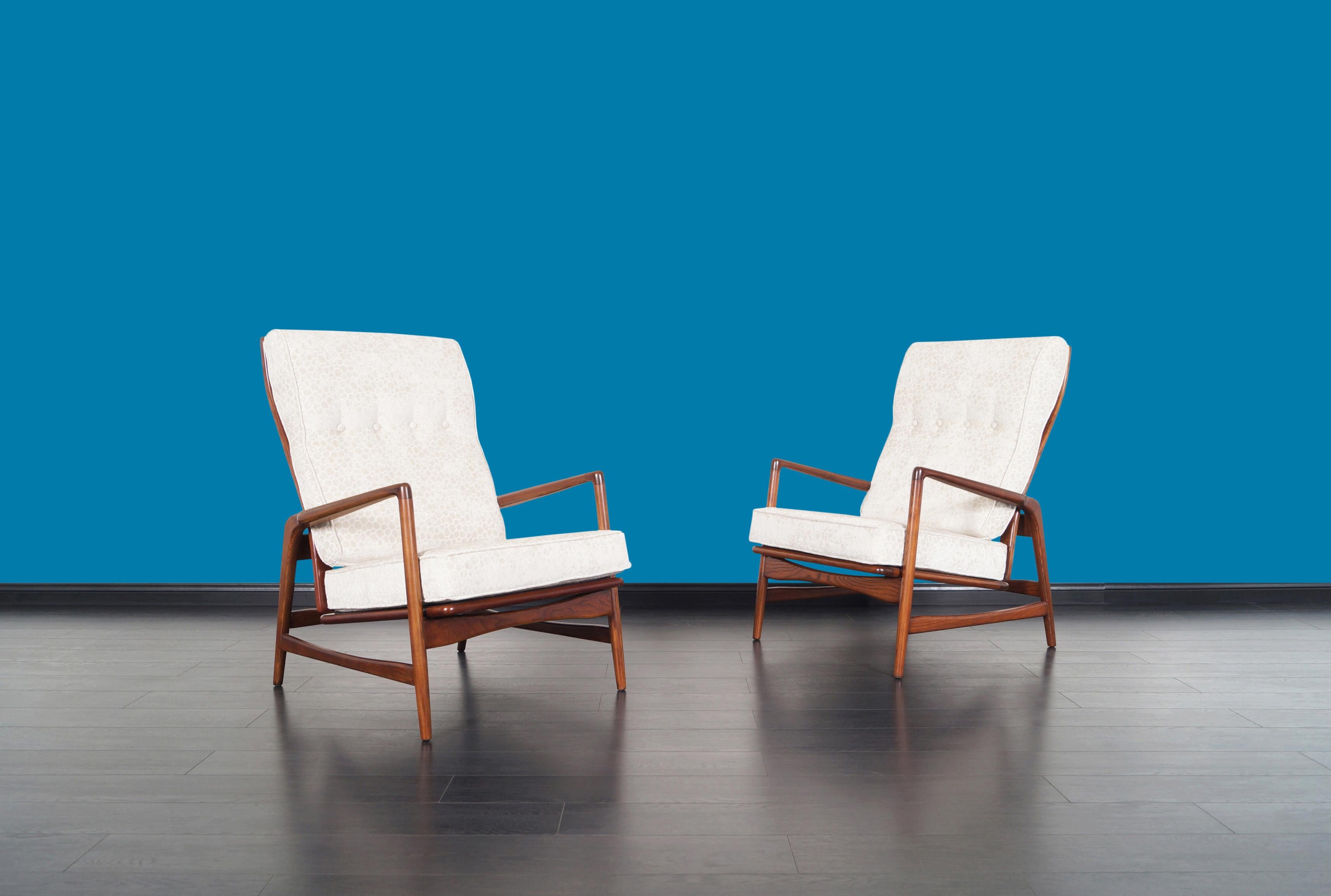 Pair of Danish high back reclining lounge chairs designed by Ib Kofod Larsen for Selig in Denmark, circa 1960s. These elegant and sculptural chairs features a solid walnut stained oak frame with sleek angled armrests. With a sculptural back, these