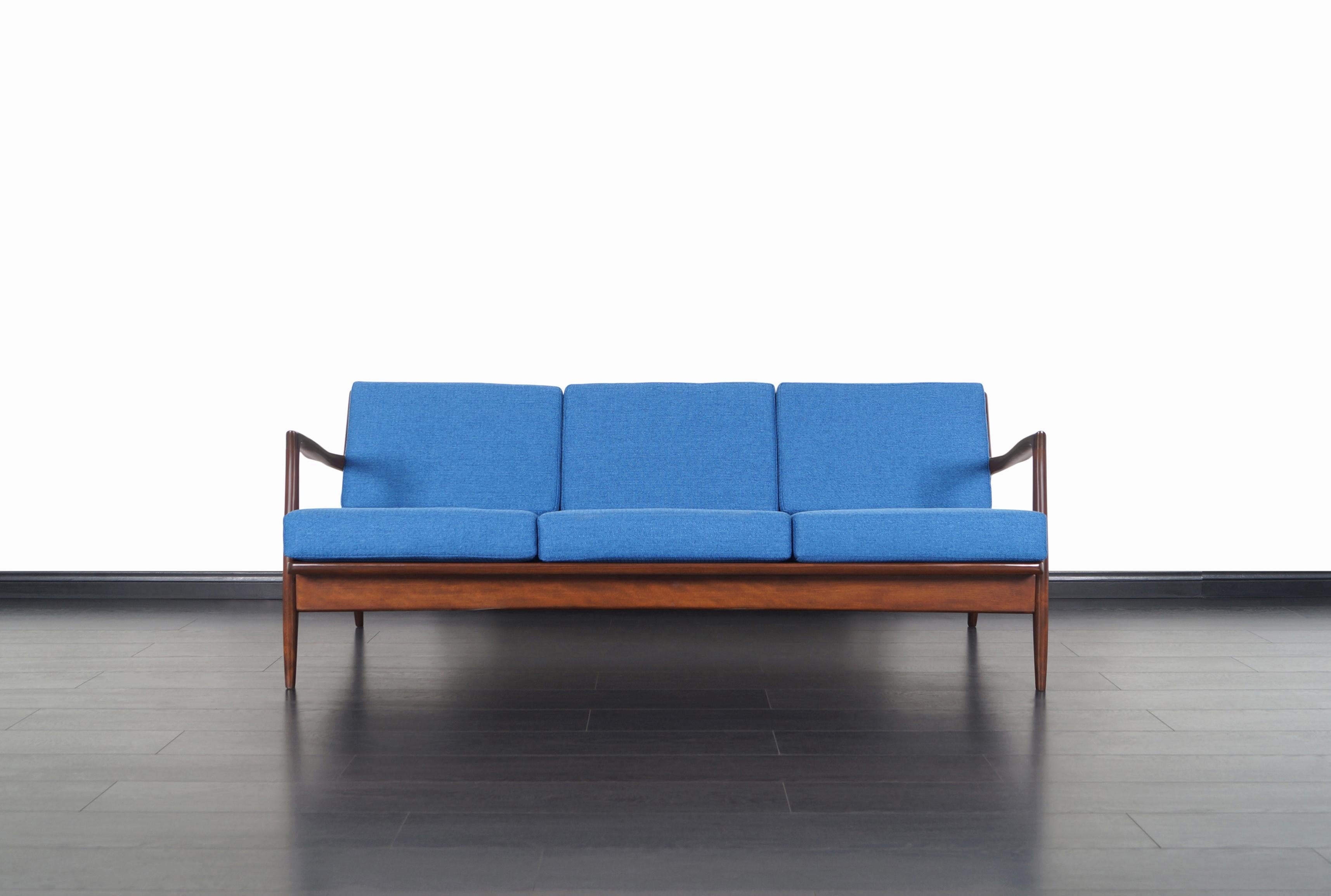 Stunning Danish modern sofa designed by architect and furniture designer Ib Kofod-Larsen for Selig in Denmark, circa 1960s. This iconic sofa features a solid walnut stained beech frame with sculptural armrests and slatted backrest. Its eye-catching