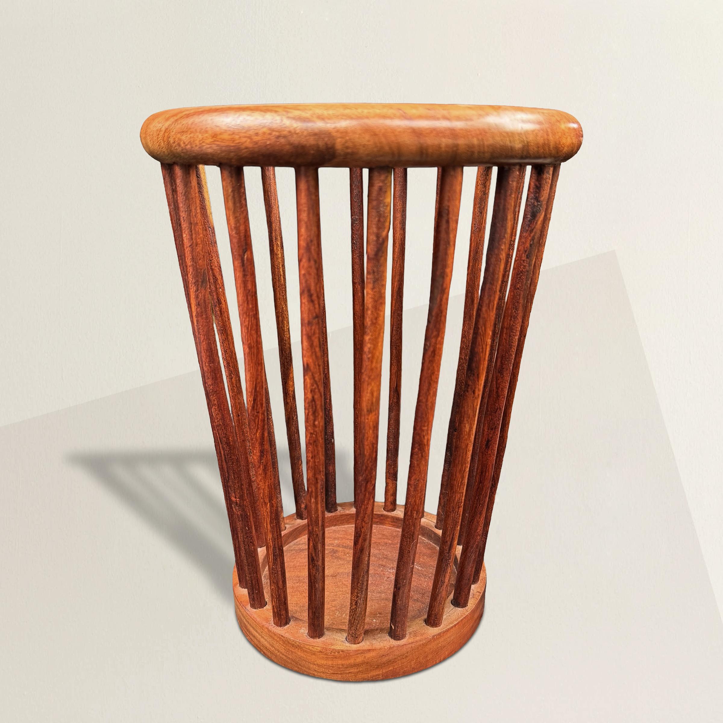 This mid-20th century Danish Modern wastepaper basket, meticulously constructed from rich mahogany, epitomizes stylish functionality. Its round ring rim, supported by elegant turned spindles, gracefully tapers down to a flat foot, creating a sleek