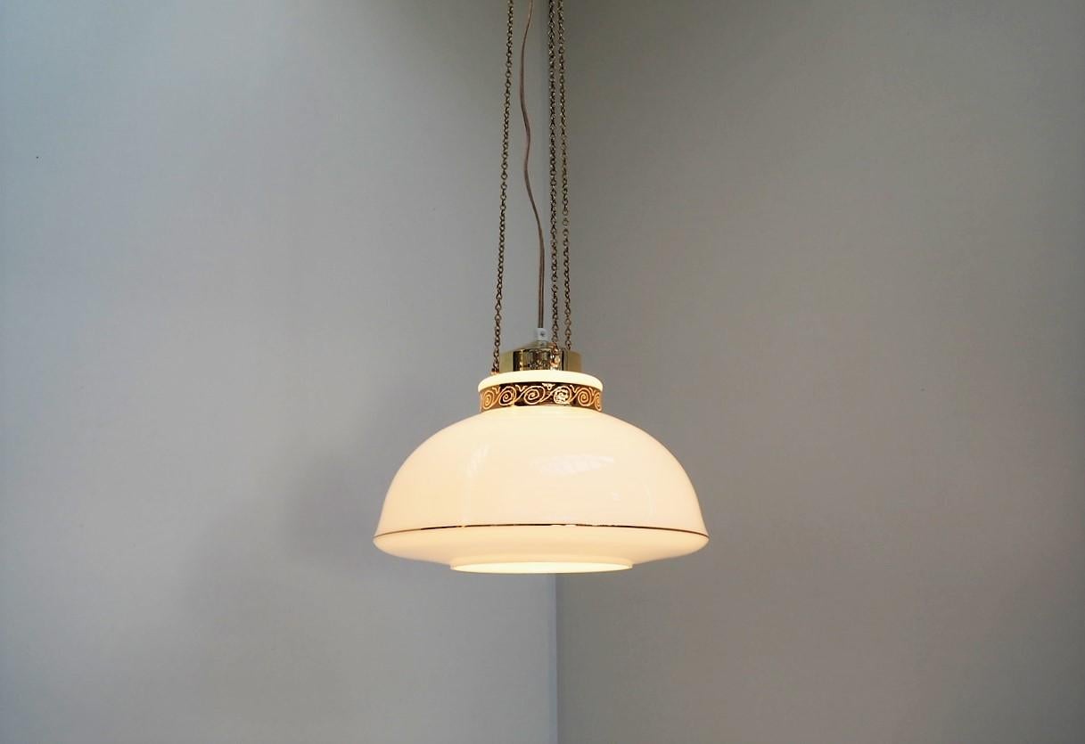 White glass pendant hanging elegantly in 3 brass chains including a suspension made in solid brass. The design gives a modern expression but still with the sought-after look of the 1960s.

The white glass shade is decorated with a gold colored