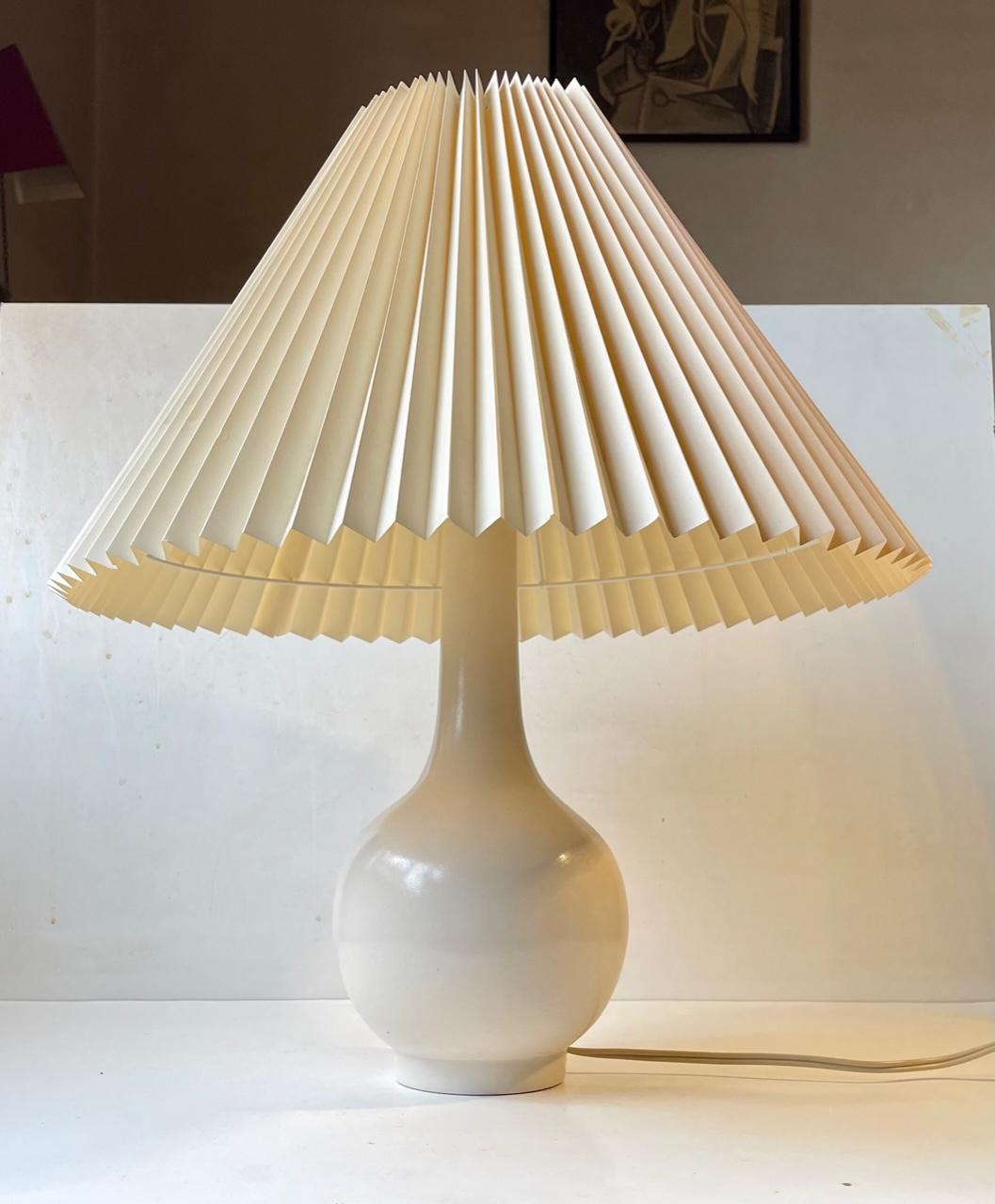 Una clásica lámpara de mesa escandinava de cerámica esmaltada. El color del esmalte es blanquecino o cáscara de huevo. Fabricada en Dinamarca hacia 1960 para C. Clausen en Svendborg. Incorpora su toma de baquelita original con interruptor de