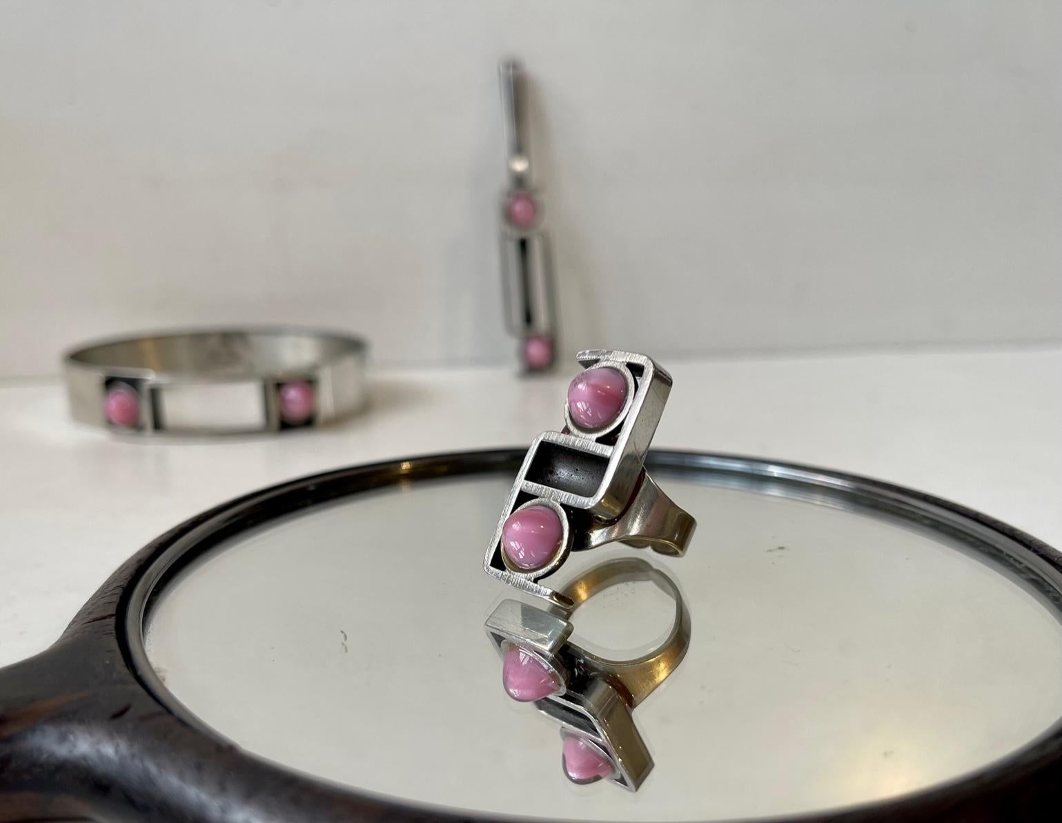 Kunstschmuck-Set bestehend aus einem mit rosa Edelsteinen besetzten Armreif, Ring und Anhänger aus Zinn. Wir vermuten, dass es sich bei den rosa Steinen entweder um Rosenquarz oder Mondsteine handelt. Dieses Set wurde in den 1970er Jahren von