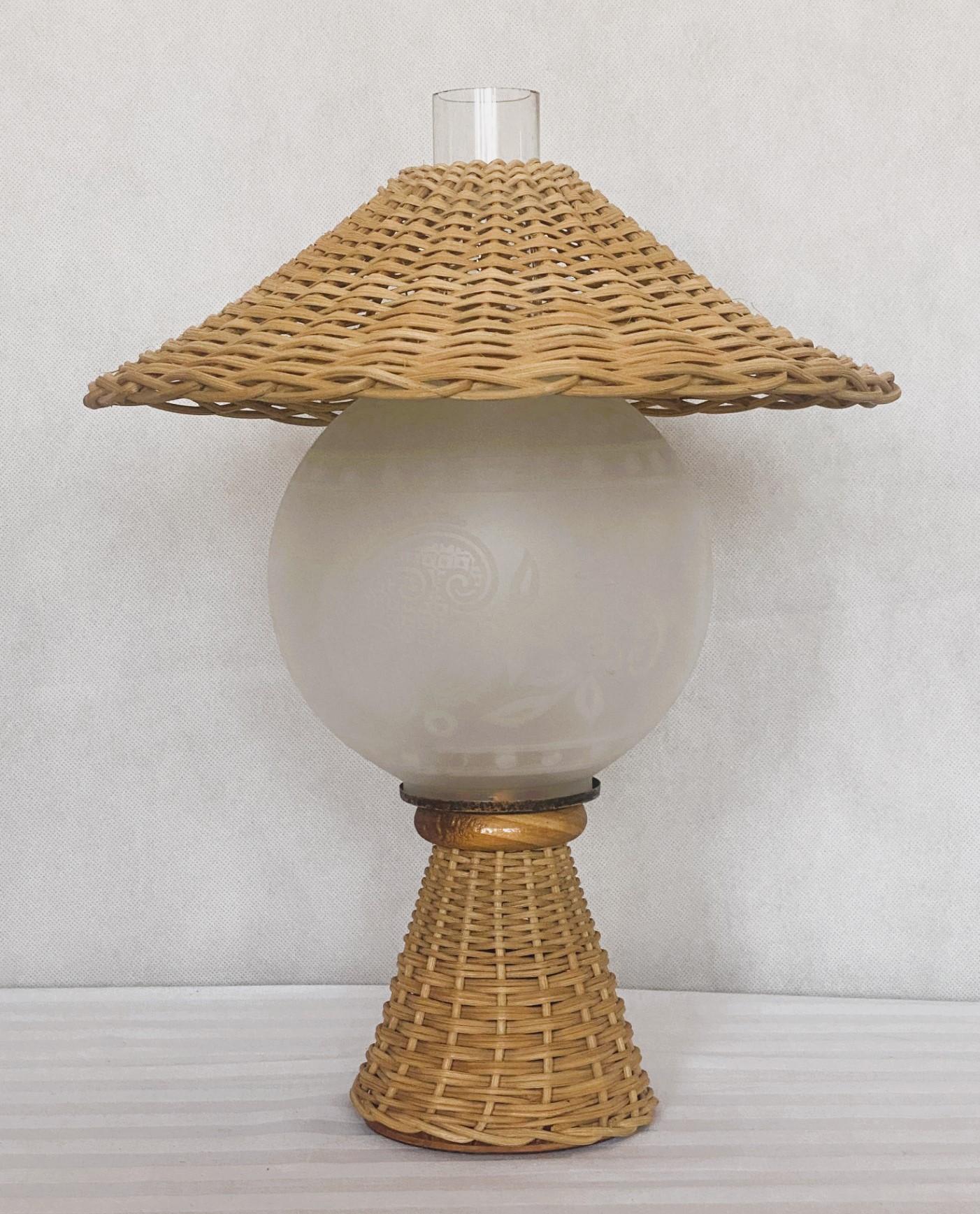 A lovely  hand-woven natural wicker table lamp manufactured in Denmark in the 1950s. Under the wicker shade with an etched glass globe with beutiful motifs and an hurrican galss. This beautiful piece is in fine vintage condition, no damages, fully