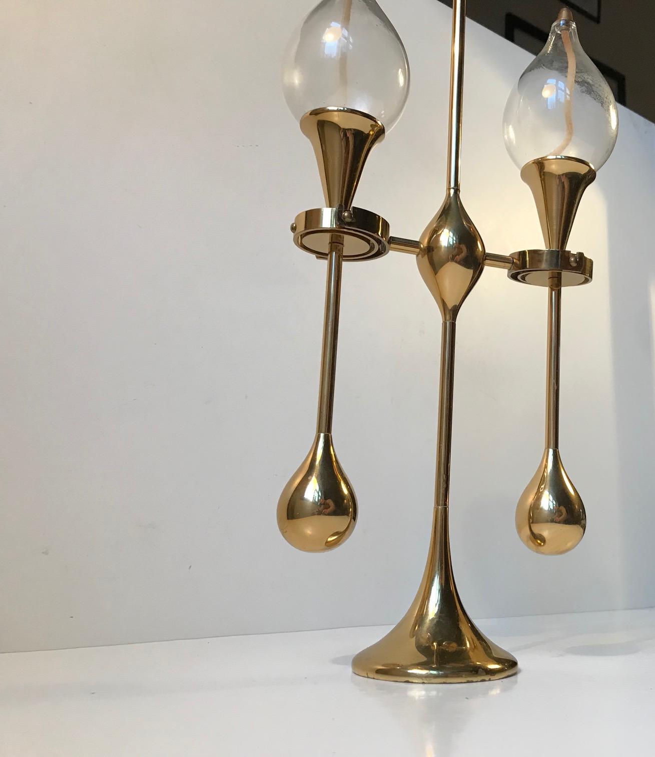 This is a large maritime hybrid table light that can function both as an oil lamp or a candle holder. It is made of polished brass and has organically drop shaped counter weights. These counter weights, together with the circular mechanisms half way