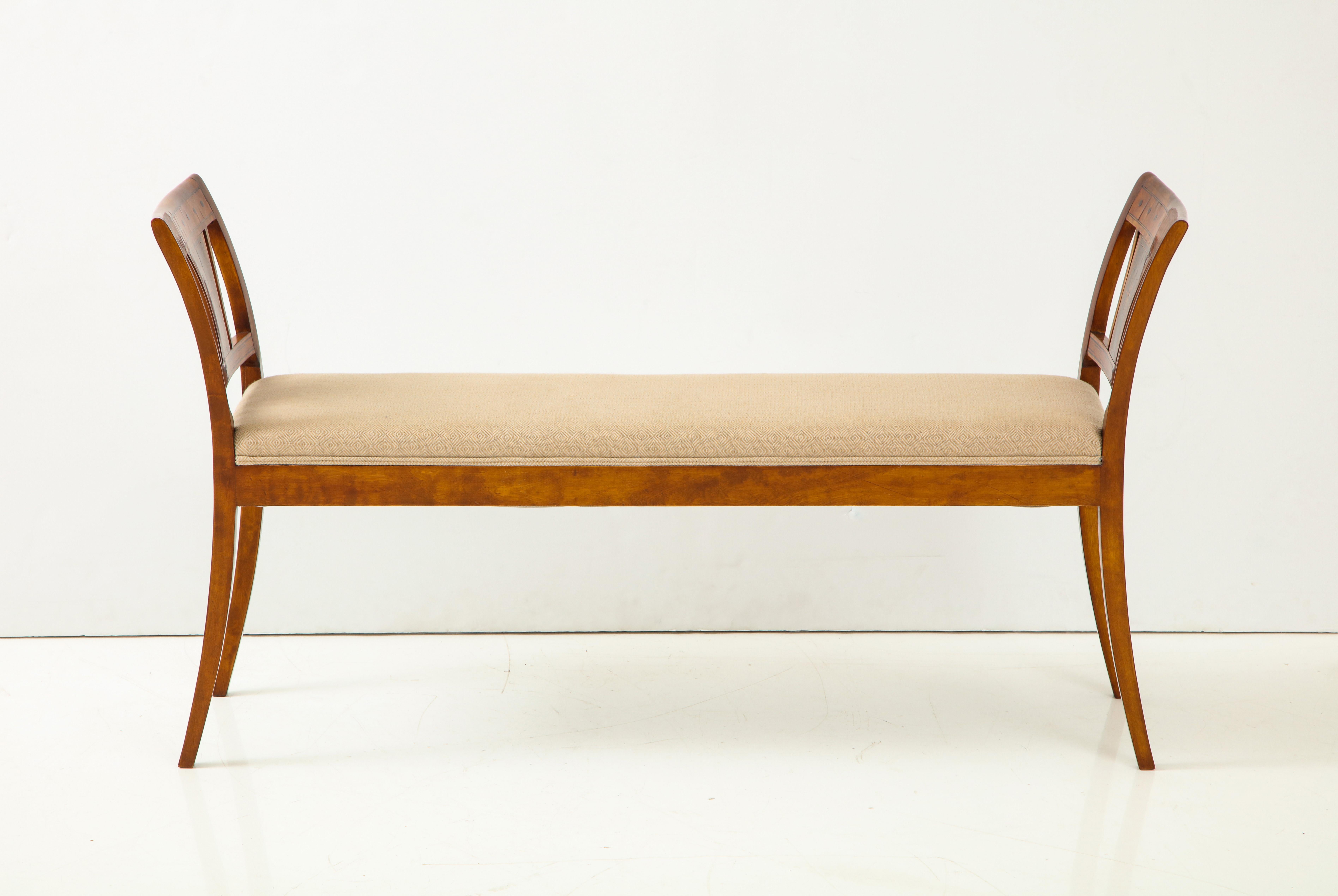 A Danish neoclassical birchwood window seat with geo-metric inlays, 19th century, with an upholstered seat between out curved armrests raised on sabre legs.