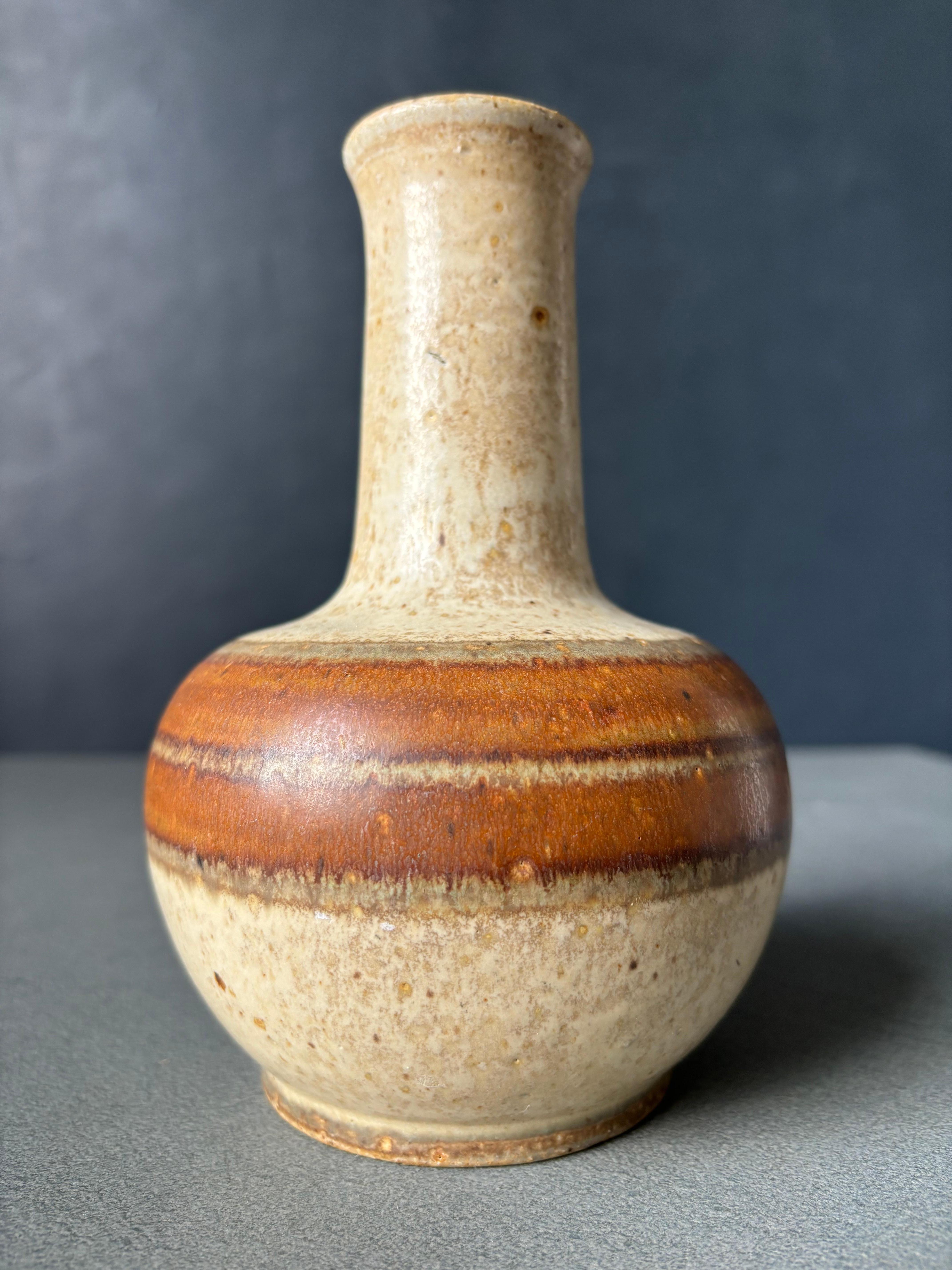 Handgedrehte dänische Vase aus der Mitte des Jahrhunderts von dem Keramikkünstler Hans Nielsen Buch (1937-2009) aus den 1960er Jahren. Sand, orange und karamellbraune Glasur. Signatur des Künstlers unter dem Sockel.
Schöner Vintage-Zustand.