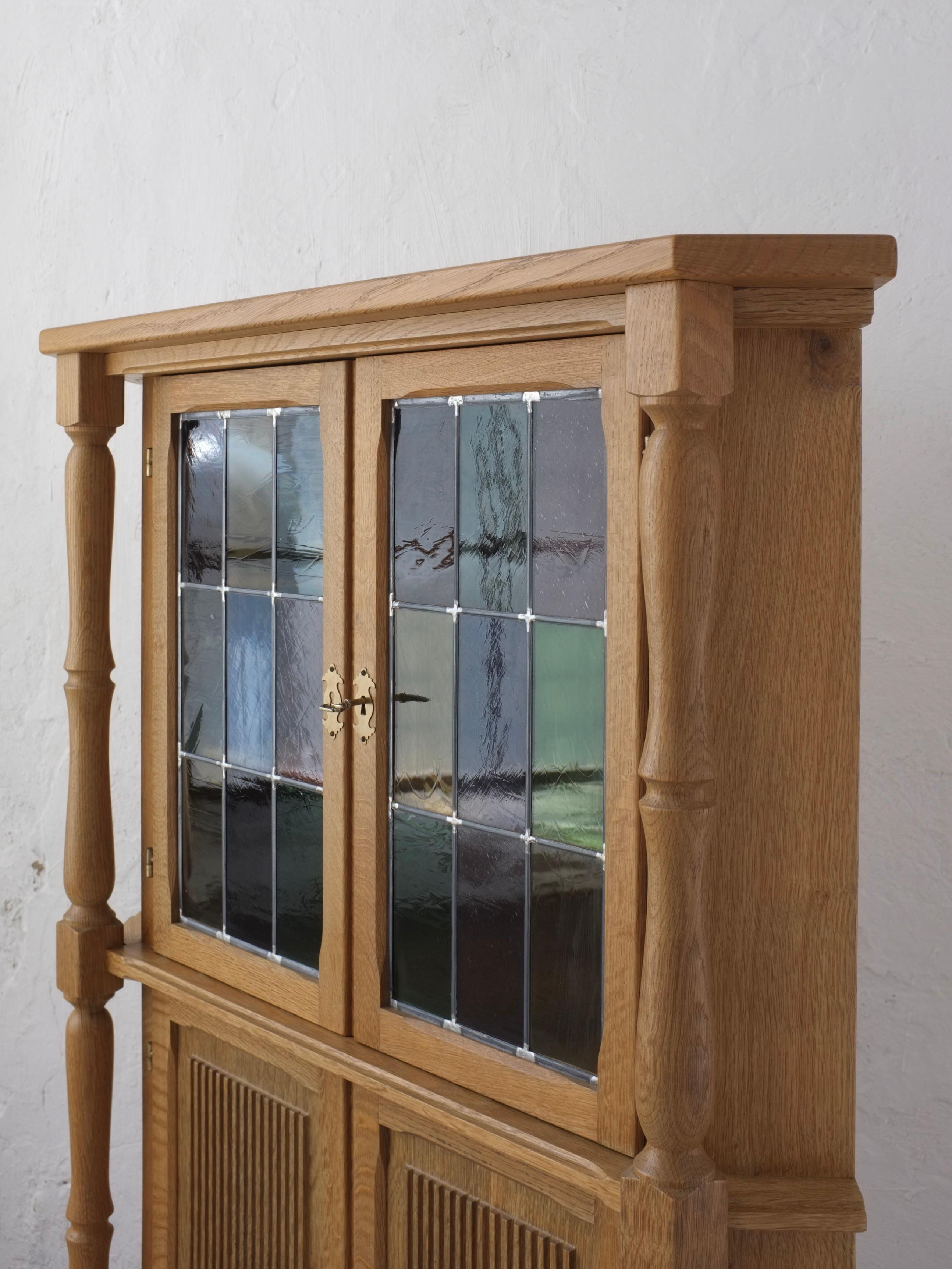 Carved oak corner cabinet with multicolor glass doors. I have a similar design sideboard by Henning Kjaernulf in stock.

Dimensions: H 140 cm, W(front) 98 cm, D 56 cm, Sides 46 cm