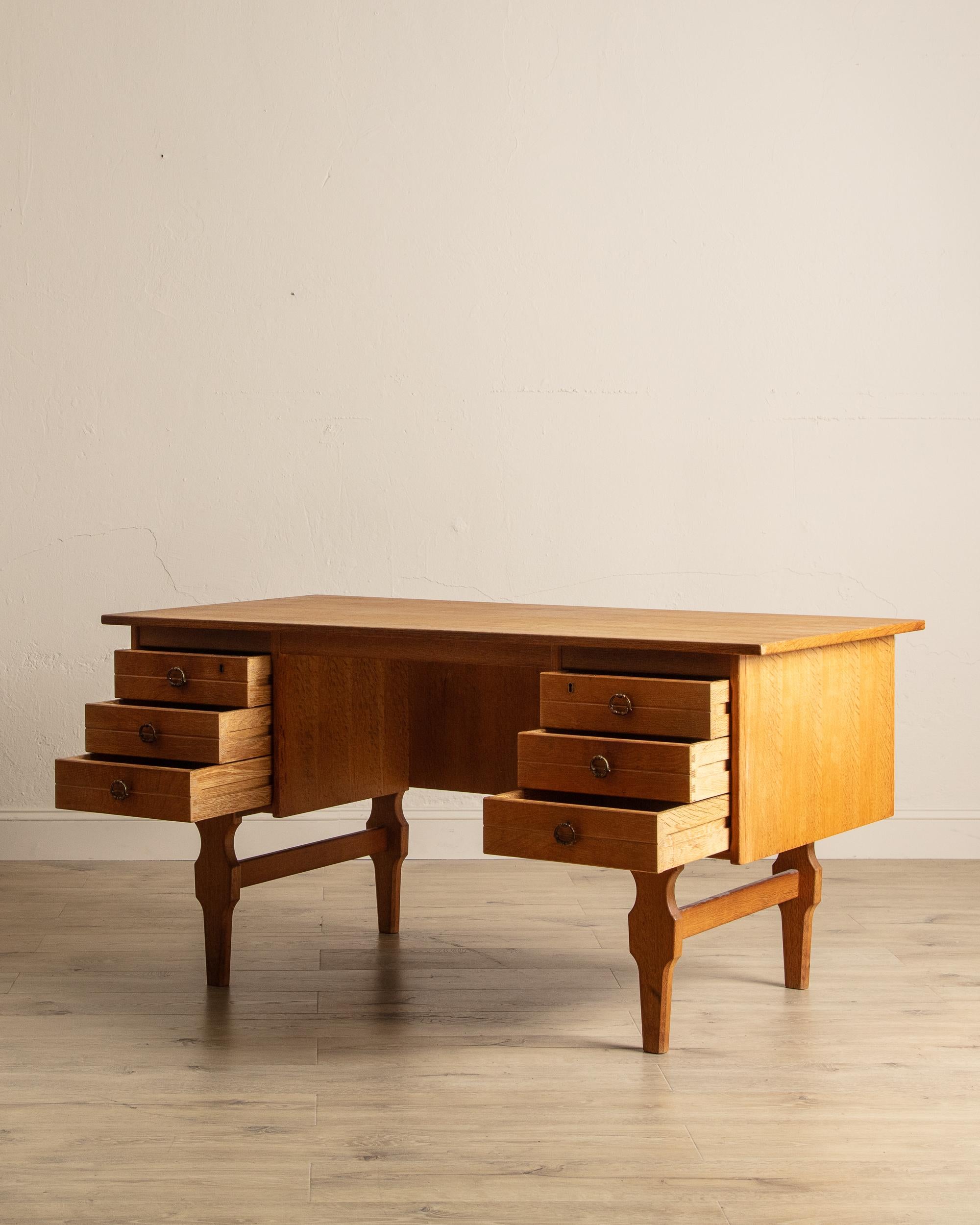 Ce bureau d'écriture en chêne danois des années 1970 présente une riche patine foncée qui met en valeur la beauté naturelle du bois et souligne son caractère vintage. Conçue dans un souci de style et de praticité, elle offre six tiroirs spacieux