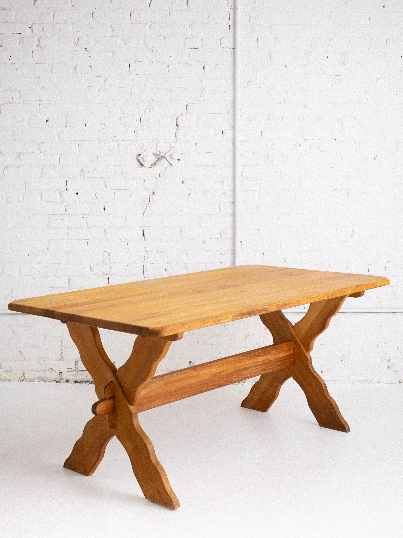 A Danish farmhouse style dining table attributed to Henning Kjaernulf. Blonde oak and trestle base with decorative scallop detail. Table can break down by removing wood pegs.