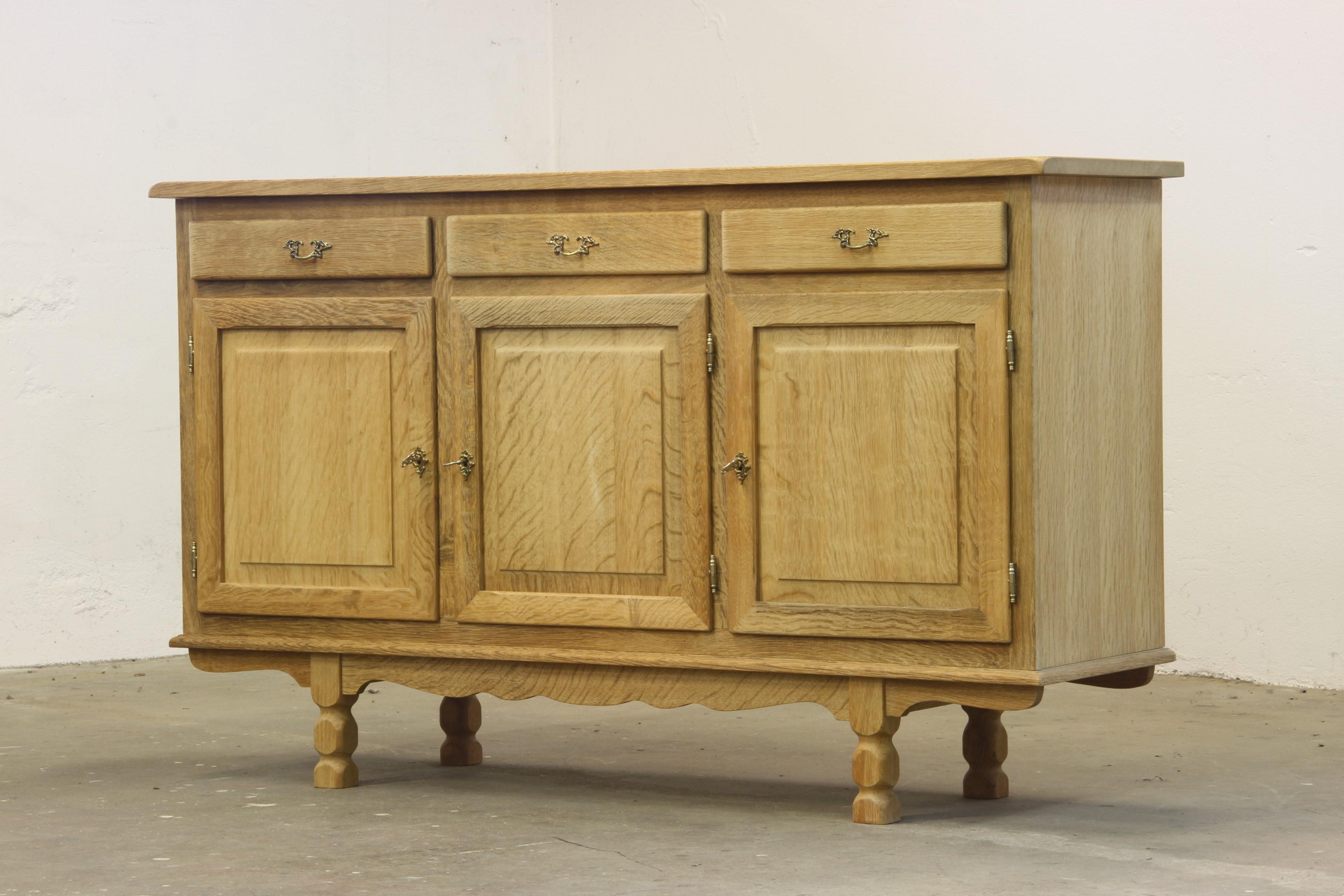 A sideboard crafted in the style of Henning Kjærnulf, showcasing oak construction with excellent craftsmanship. It features adjustable shelving with corner holes in the back frame, combining functionality with a thoughtful design.

The surface was
